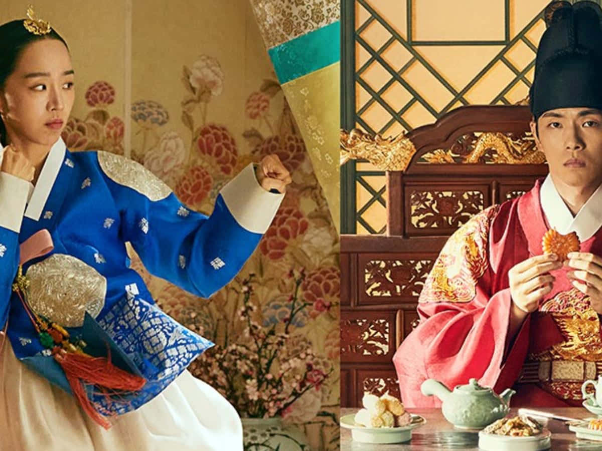 女王 桌布 壁紙 — 一名身穿藍色韓服的女性在華麗的宮殿房間裡，在一位身穿紅色韓服、正在吃零食的男性旁邊擺出武術姿勢。
