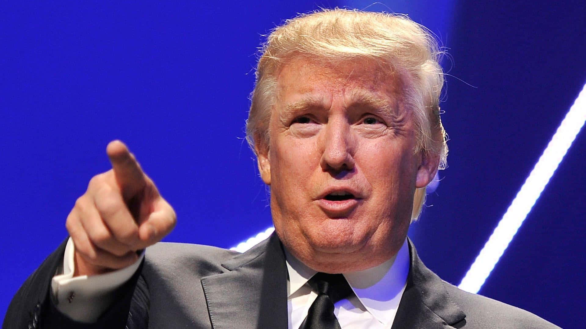 trump 桌布 壁紙 — 一名身穿西裝的男子在充滿活力的藍色背景和明亮的白色對角燈光下向前指。