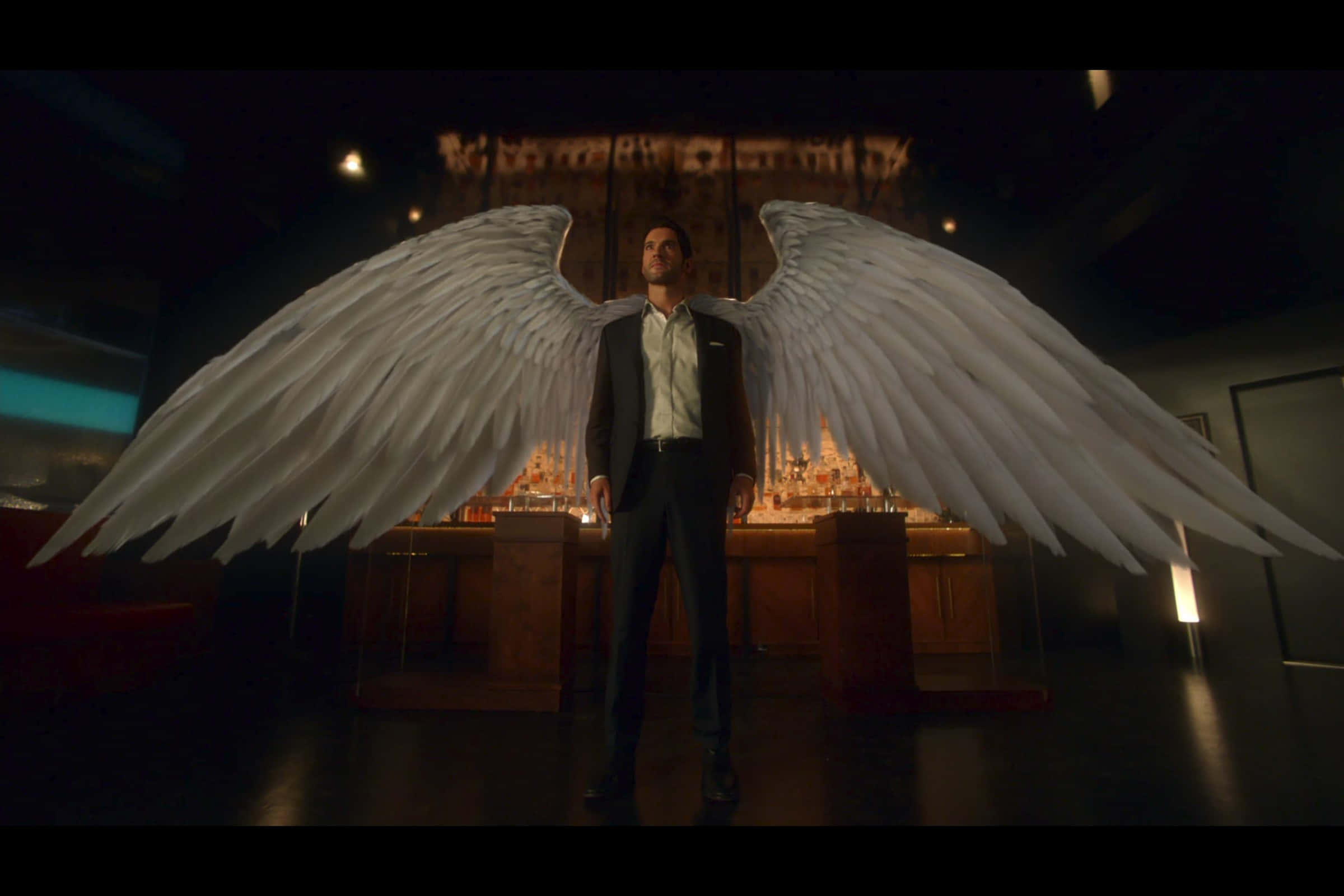 Lucifer Wings 桌布 壁紙 — 一名身穿西裝的男子在燈光昏暗、裝飾華麗的房間中張開巨大的白色天使翅膀。