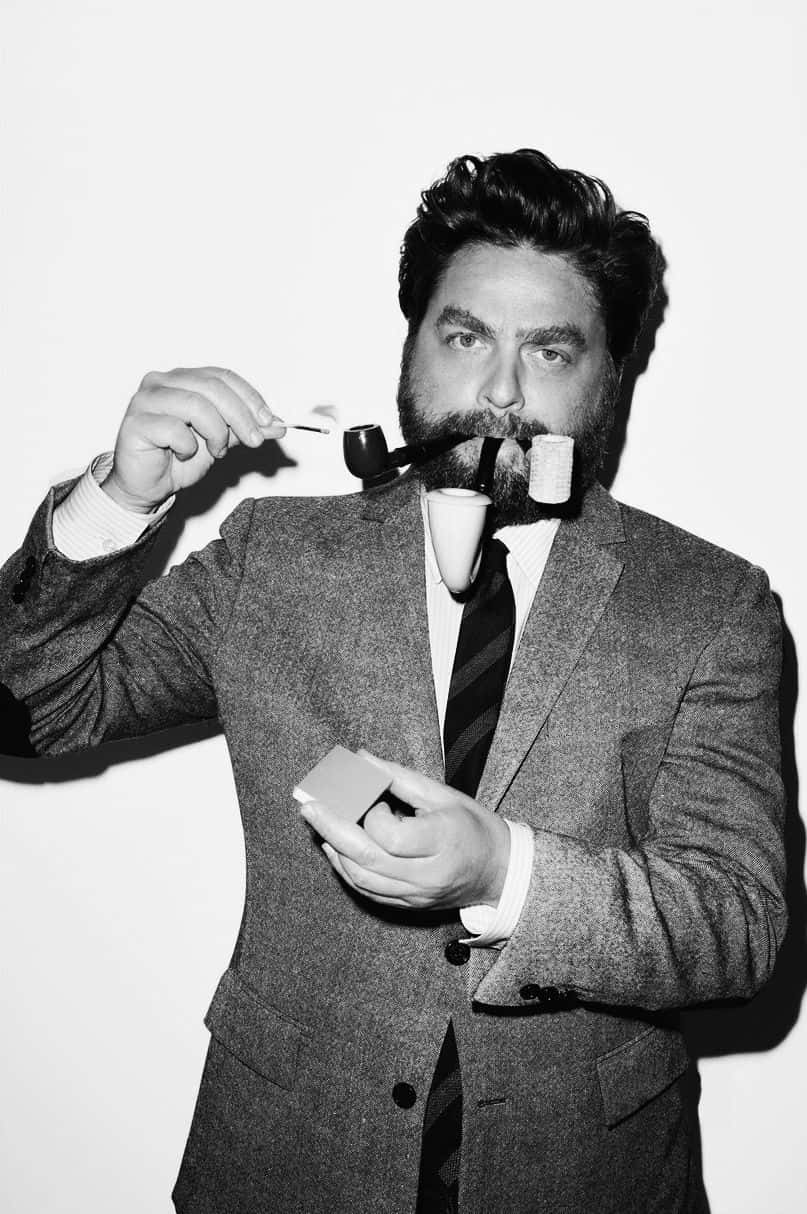 Zach Galifianakis 桌布 壁紙 — 一名身穿西裝的男子在純白背景下，於戲劇性的黑白肖像中，將點燃的火柴湊近他的煙斗。