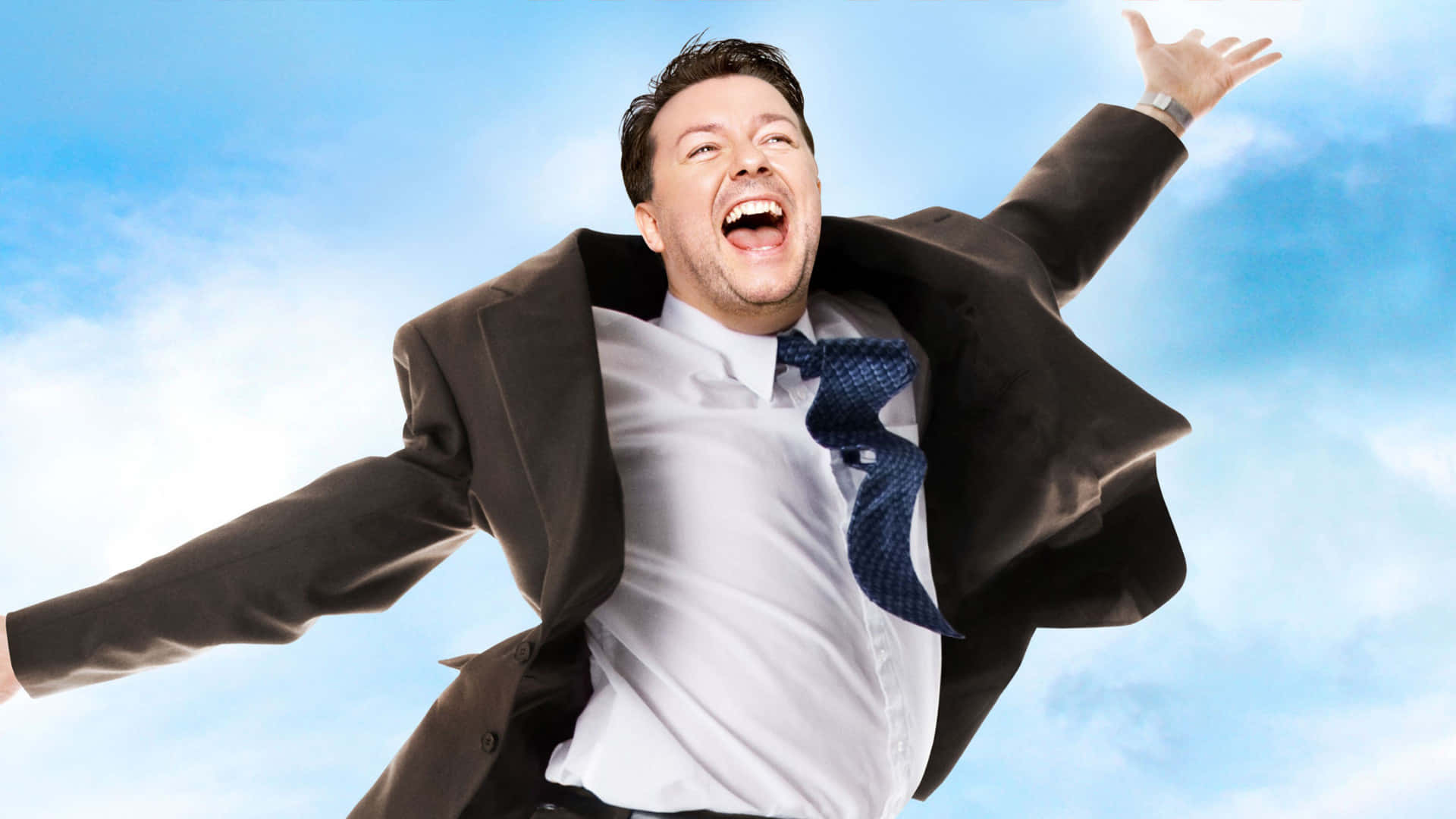 ricky gervais 桌布 壁紙 — 一名身穿西裝的男子在藍天白雲下歡快地跳躍。