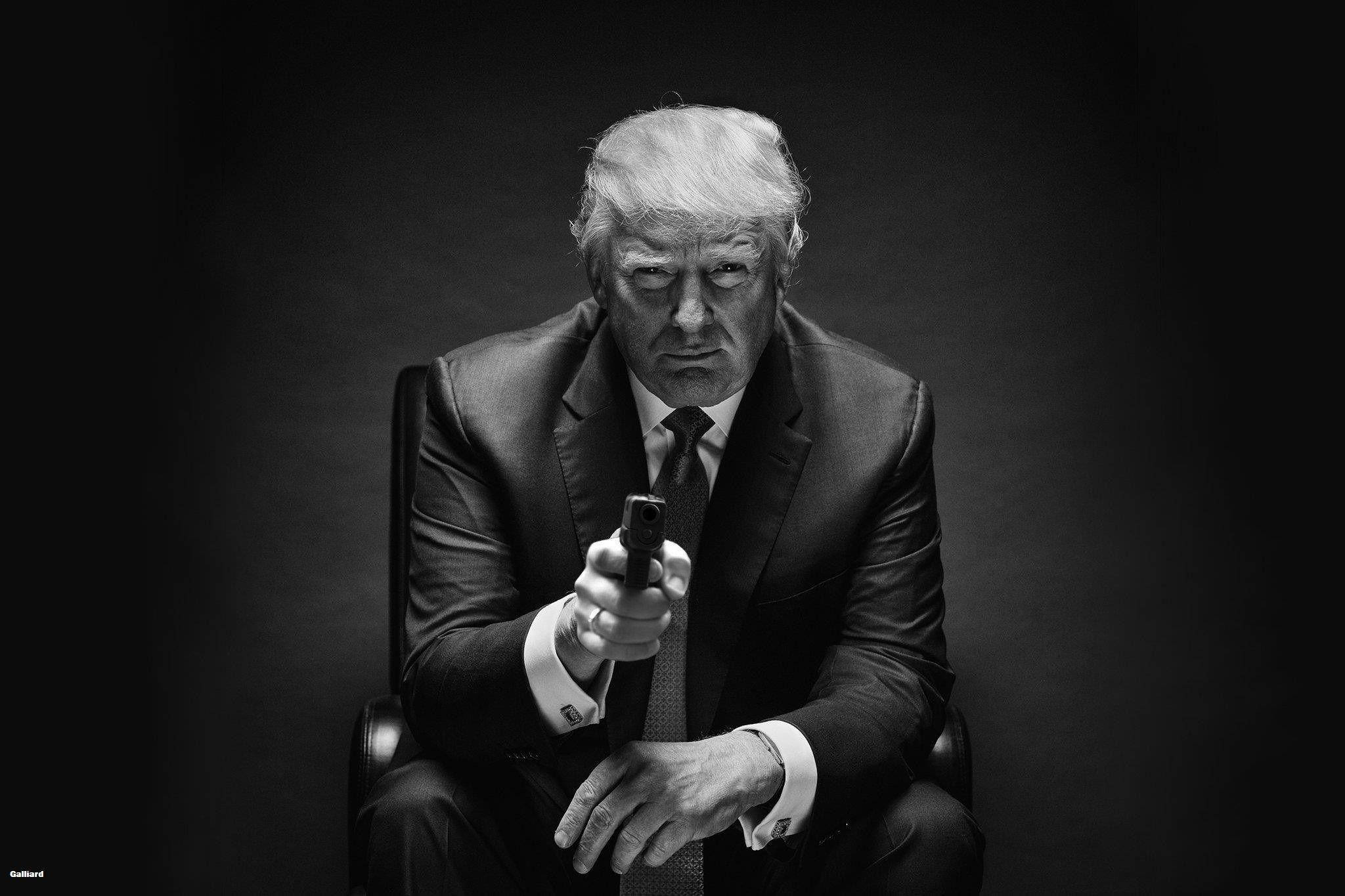 donald trump 桌布 壁紙 — 一名身穿西裝的男子坐在椅子上，手持手槍指向觀眾，呈現鮮明的黑白肖像。
