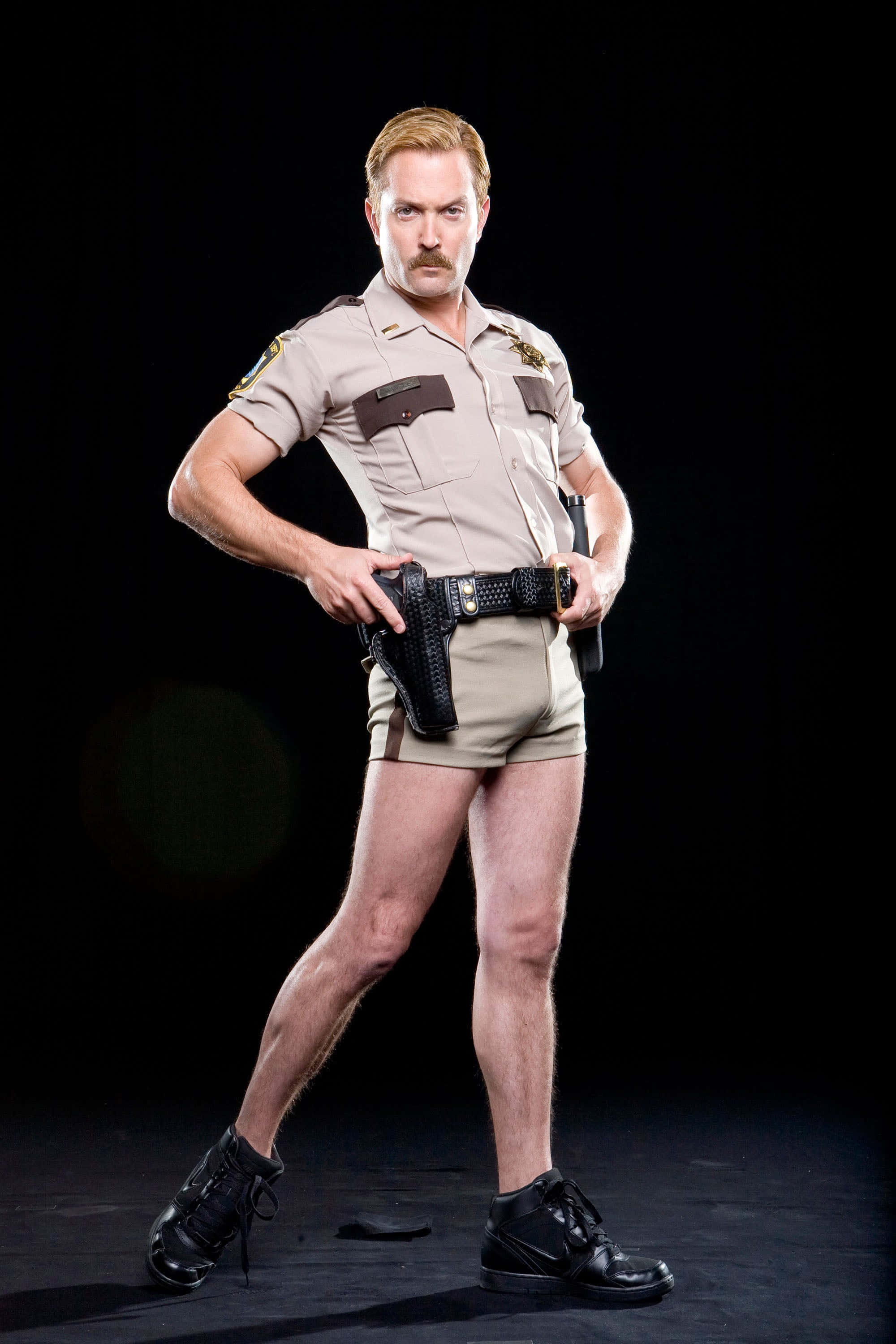 thomas lennon 桌布 壁紙 — 一名身穿警長制服、短褲和靴子的男子在黑色背景前自信地擺姿勢。
