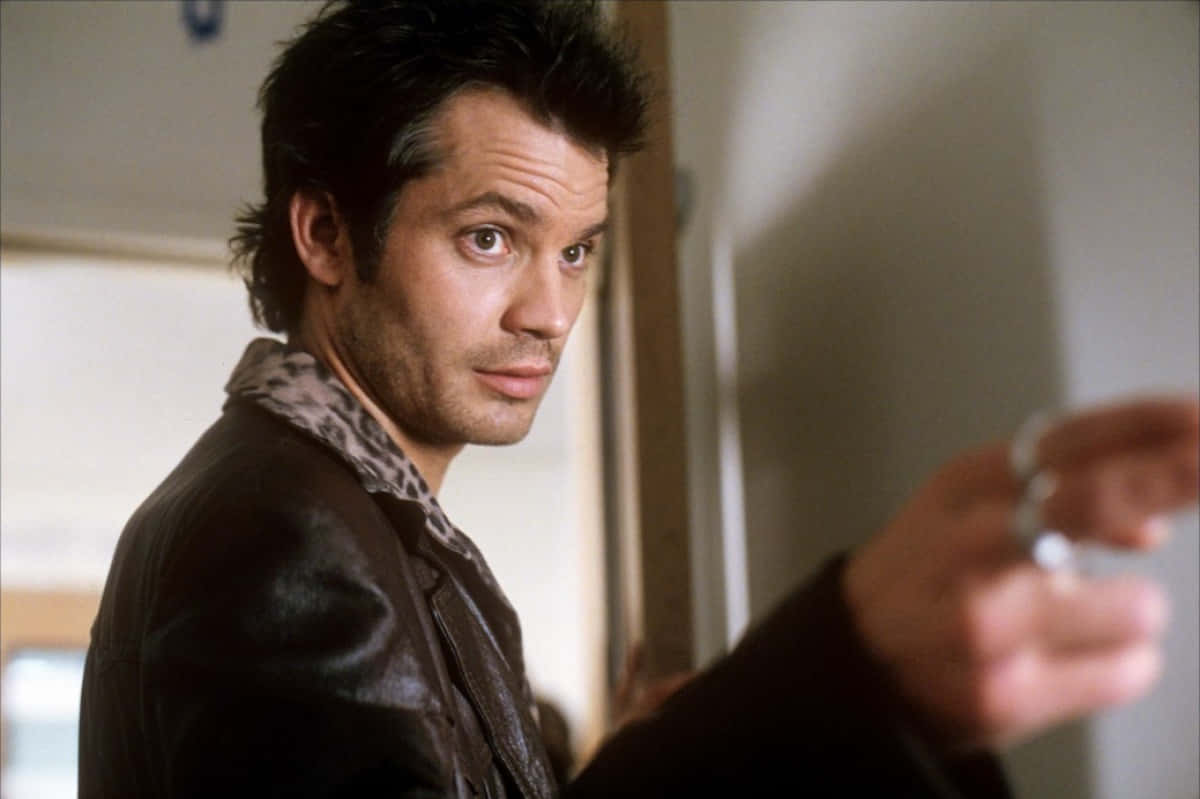 timothy olyphant 桌布 壁紙 — 一名身穿豹紋領皮褸的男子，在柔和光線的室內環境中，表情嚴肅地向前指。