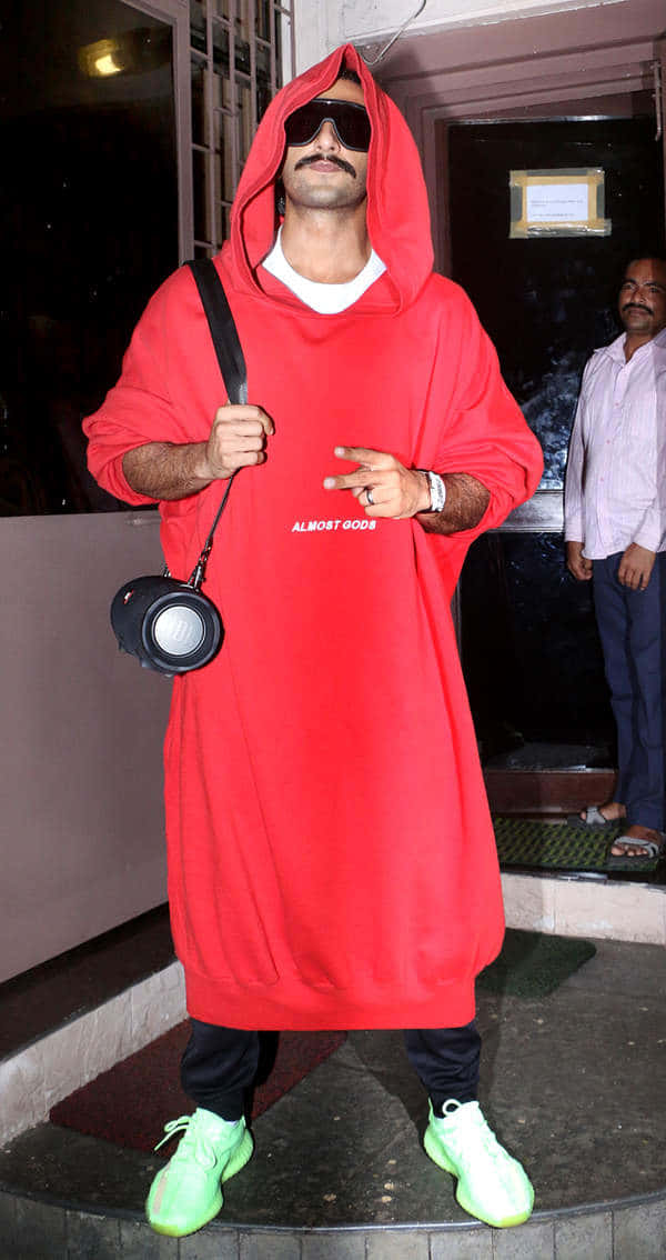 Red Hoodie 桌布 壁紙 — 一名身穿超大紅色連帽衫和螢光綠色運動鞋的男子，在夜間自信地拿著相機包擺姿勢。