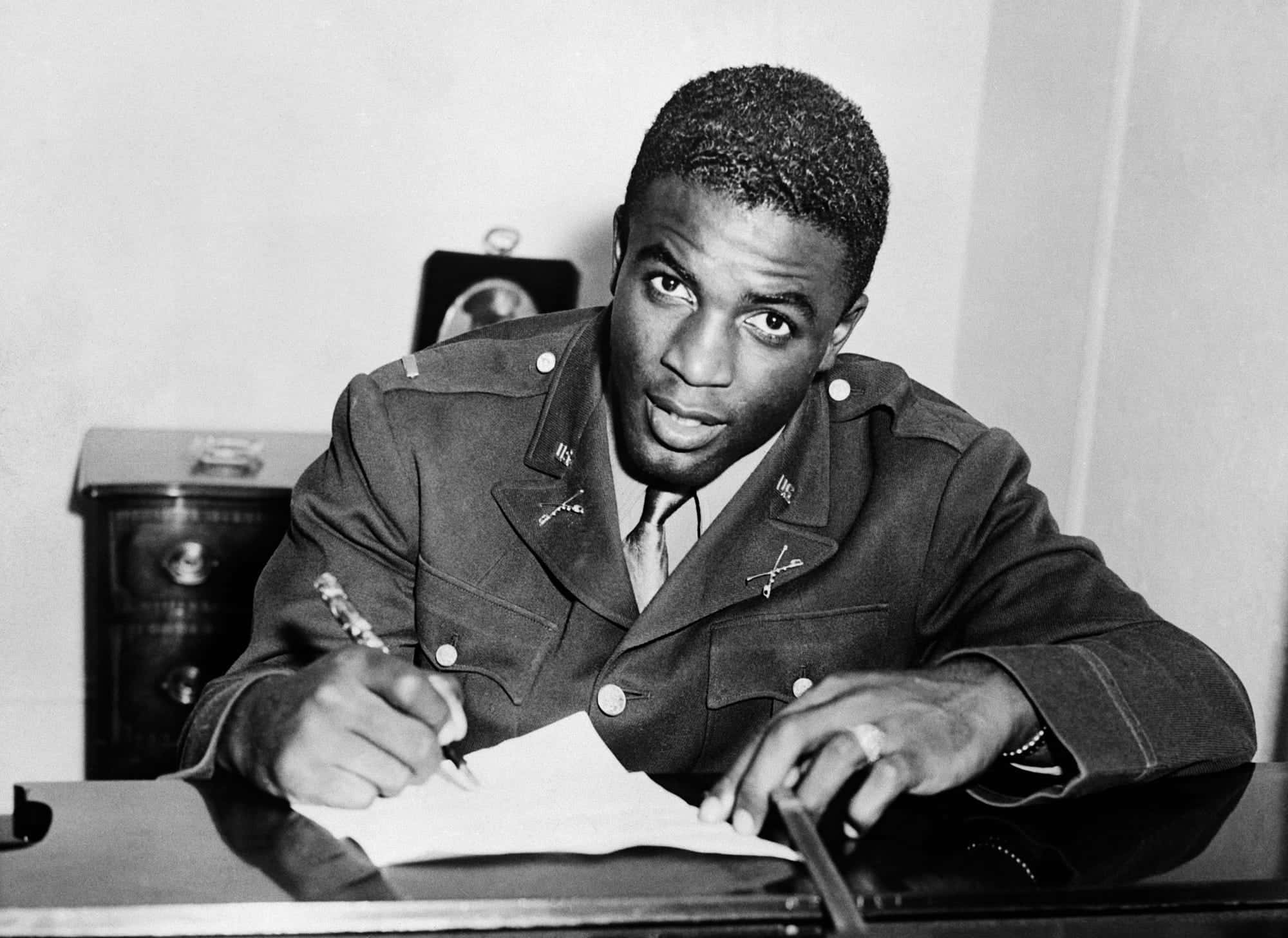 Jackie Robinson 桌布 壁紙 — 一名身穿軍裝的年輕黑人男子坐在桌前，用筆簽署文件，同時直視鏡頭。