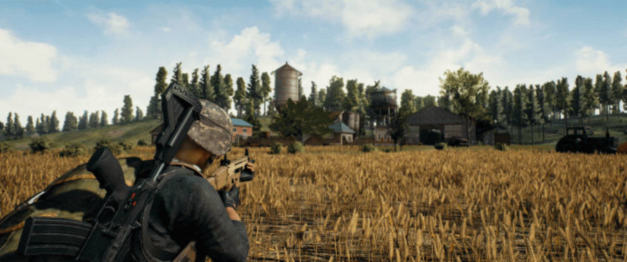 PUBG 桌布 壁紙 — 一名身穿迷彩服的士兵蹲在金黃色的麥田裡，在明亮的藍天下用步槍瞄準遠處的農莊。