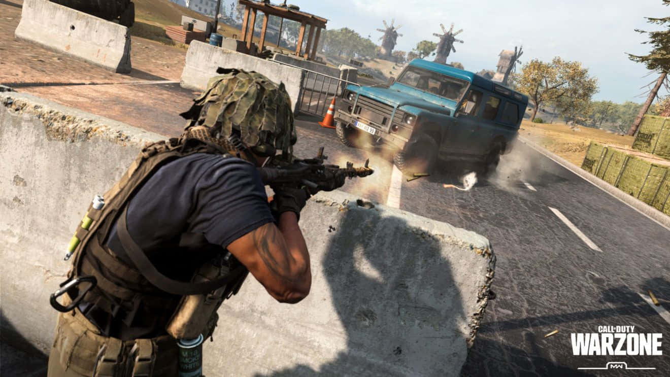 Call Of Duty Vehicles 桌布 壁紙 — 一名身穿迷彩裝備的士兵在混凝土屏障後開步槍，一輛藍色貨車在陽光照耀的道路上爆炸。