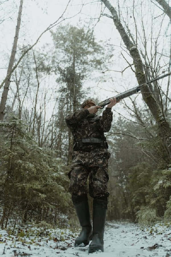 Snowshoes 桌布 壁紙 — 一名身穿迷彩裝備的獵人，在白雪覆蓋的冬季森林中，透過光禿的樹木和常綠植物瞄準獵槍。