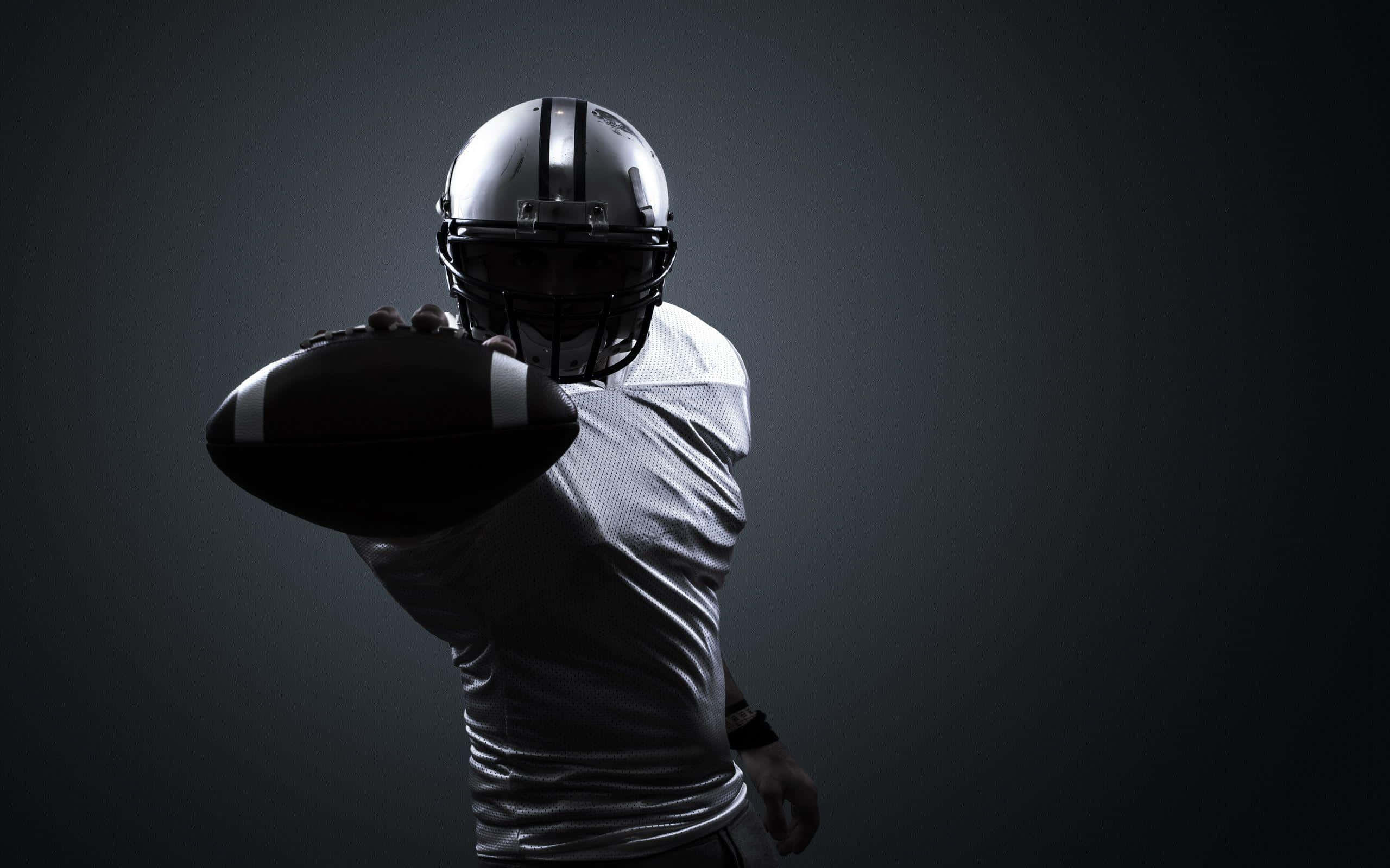 Cool Football 桌布 壁紙 — 一名身穿銀色頭盔和球衣的美式足球員準備在深色漸變背景前投球。