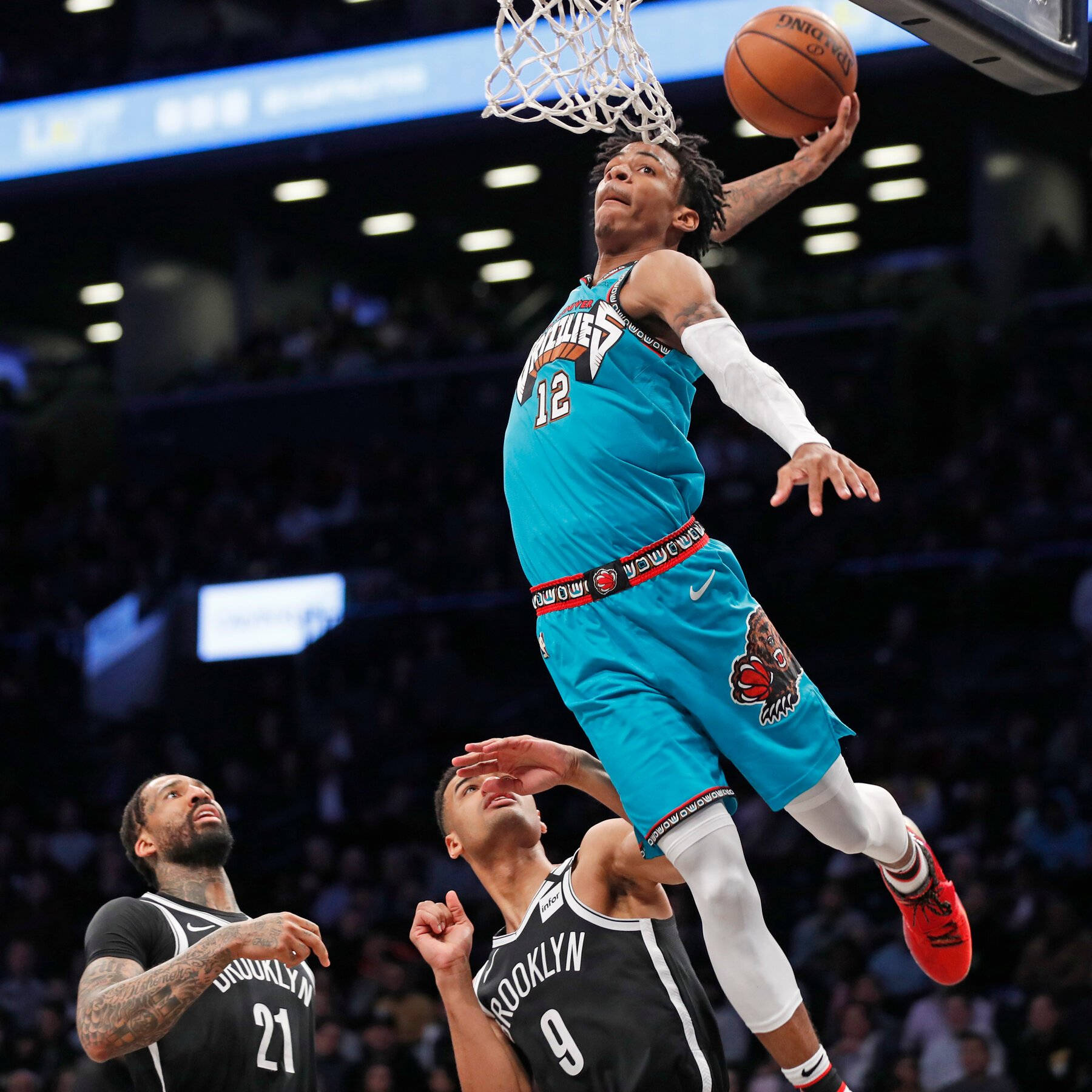 Ja Morant 入樽 桌布 壁紙 — 一名身穿青綠色球衣的籃球運動員入樽，兩名身穿黑色球衣的防守球員在下方觀看。