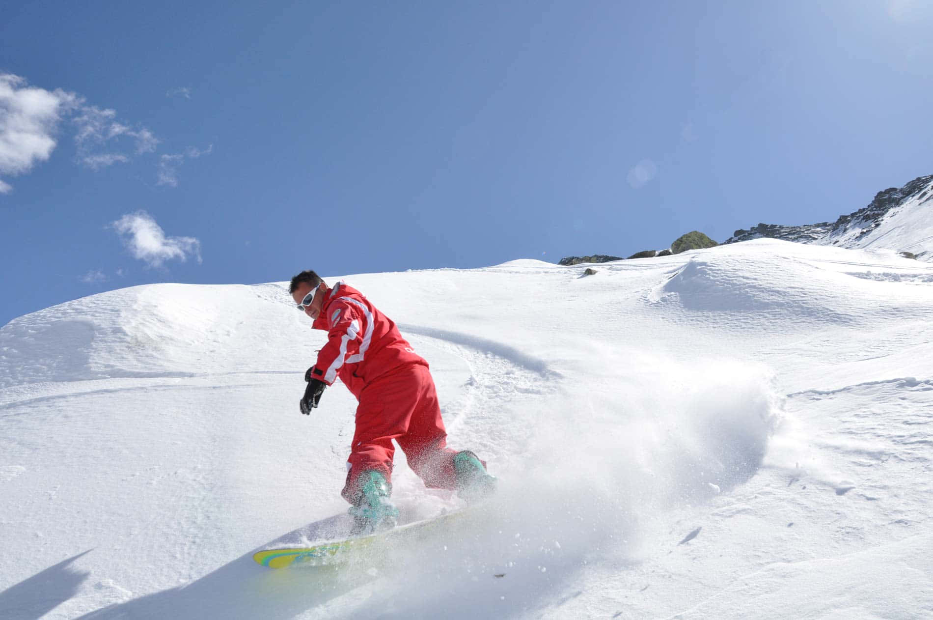 Skiing 桌布 壁紙 — 一名身穿鮮紅色套裝的滑雪板運動員在陽光明媚的雪山斜坡上劃過新鮮的粉雪。