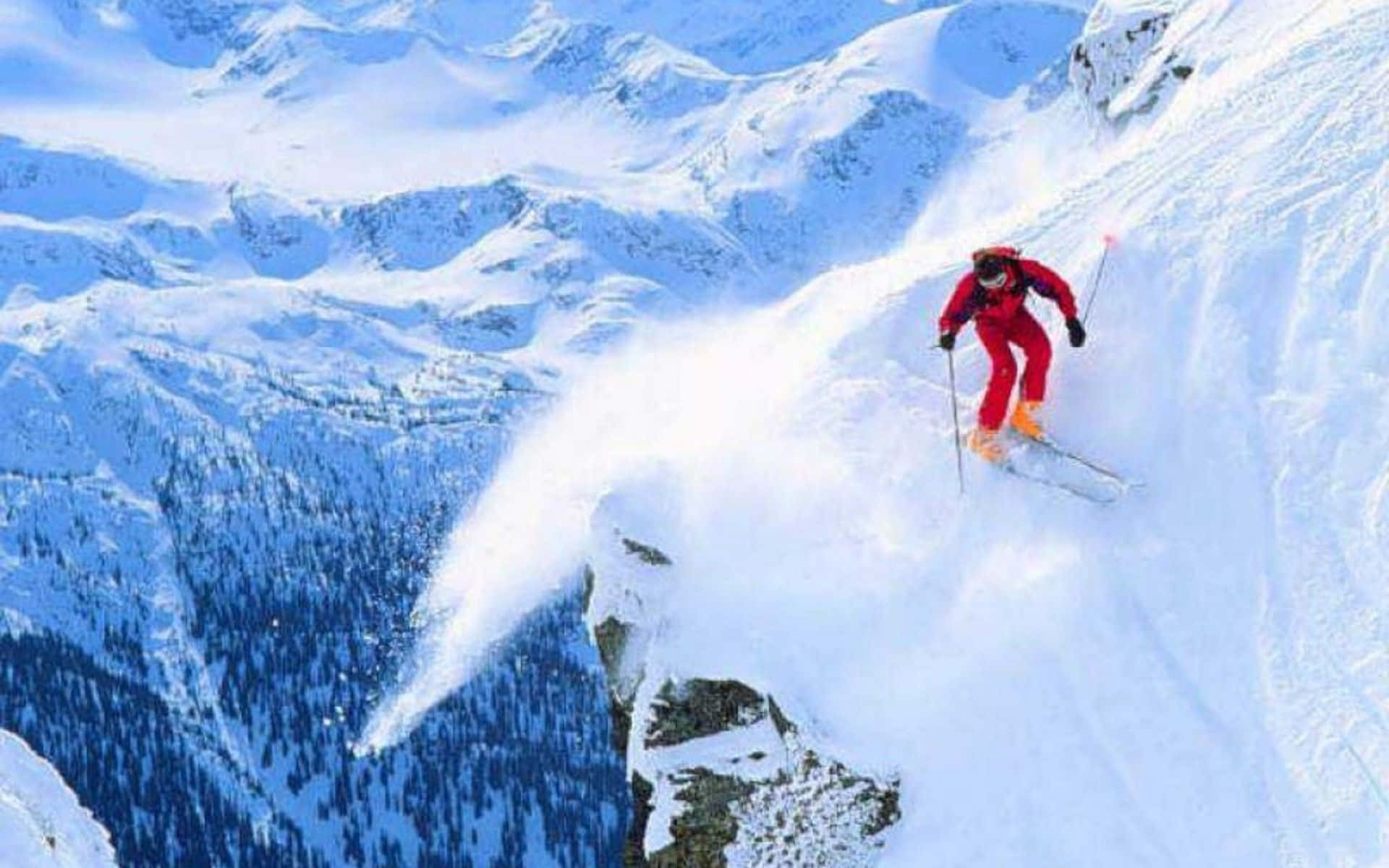 Winter Sports 桌布 壁紙 — 一名身穿鮮紅色滑雪服的滑雪者，在陡峭的雪山斜坡上刻滑，揚起一陣粉雪。