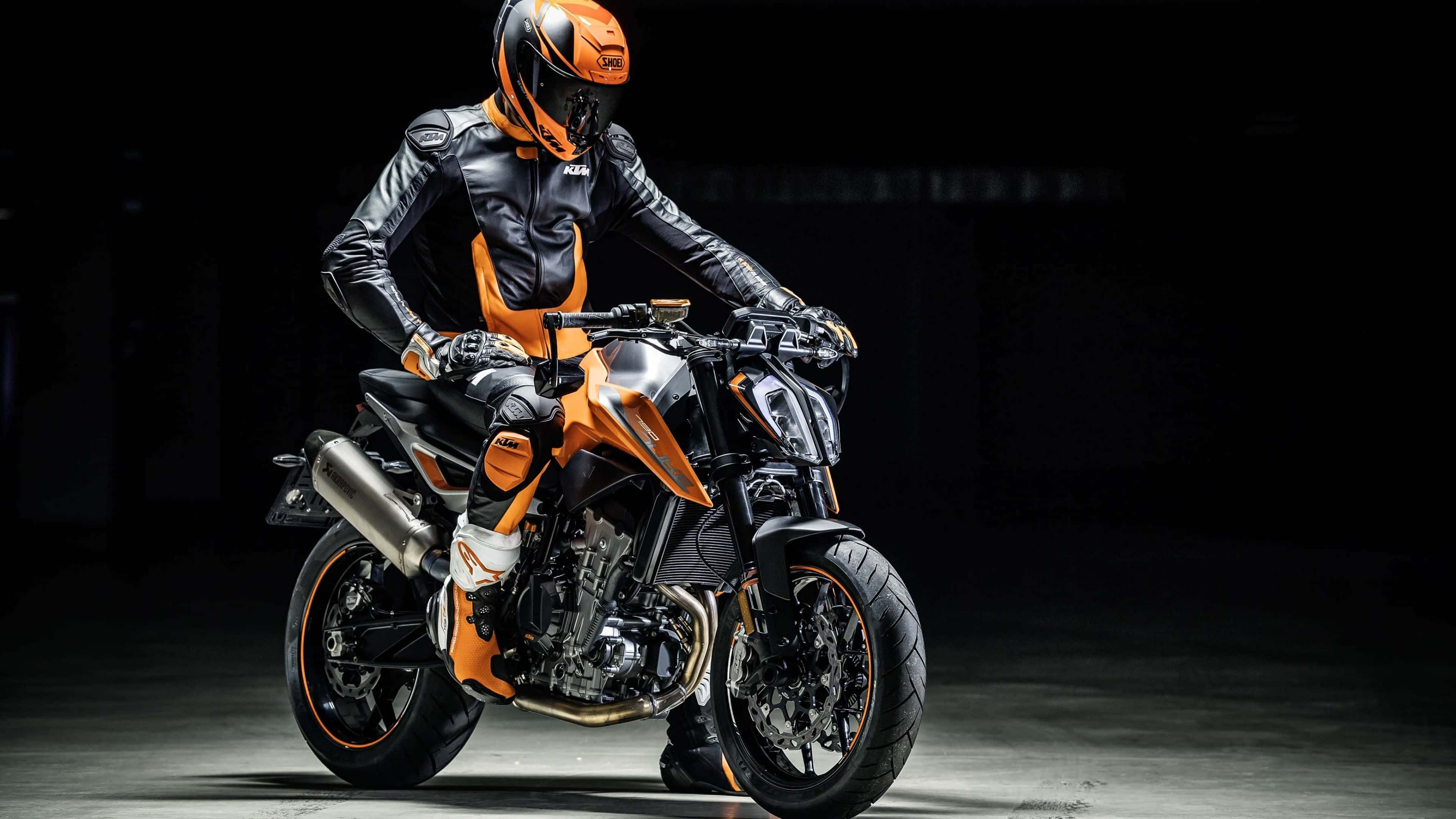 Ktm Bike 桌布 壁紙 — 一名身穿黑橙色裝備的騎士，在戲劇性的工作室燈光下，坐在流線型的KTM電單車上，蓄勢待發。