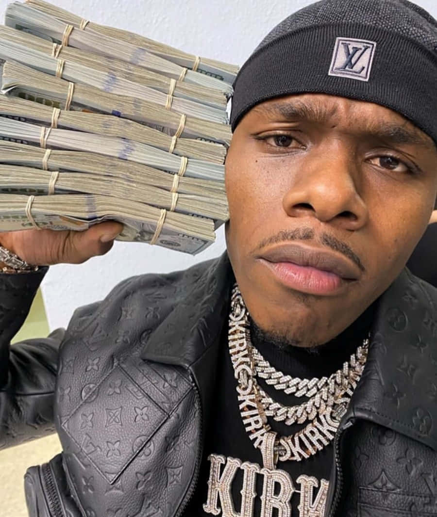 Dababy 桌布 壁紙 — 一名身穿黑色Louis Vuitton外套和冷帽的男子，手持一大疊捆好的現金，專注地凝視鏡頭。