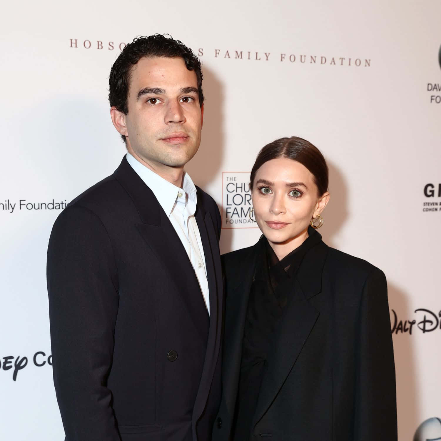 ashley olsen 桌布 壁紙 — 一名身穿黑色正裝的男士和女士在白色背景上帶有標誌的慈善活動中一起擺姿勢。