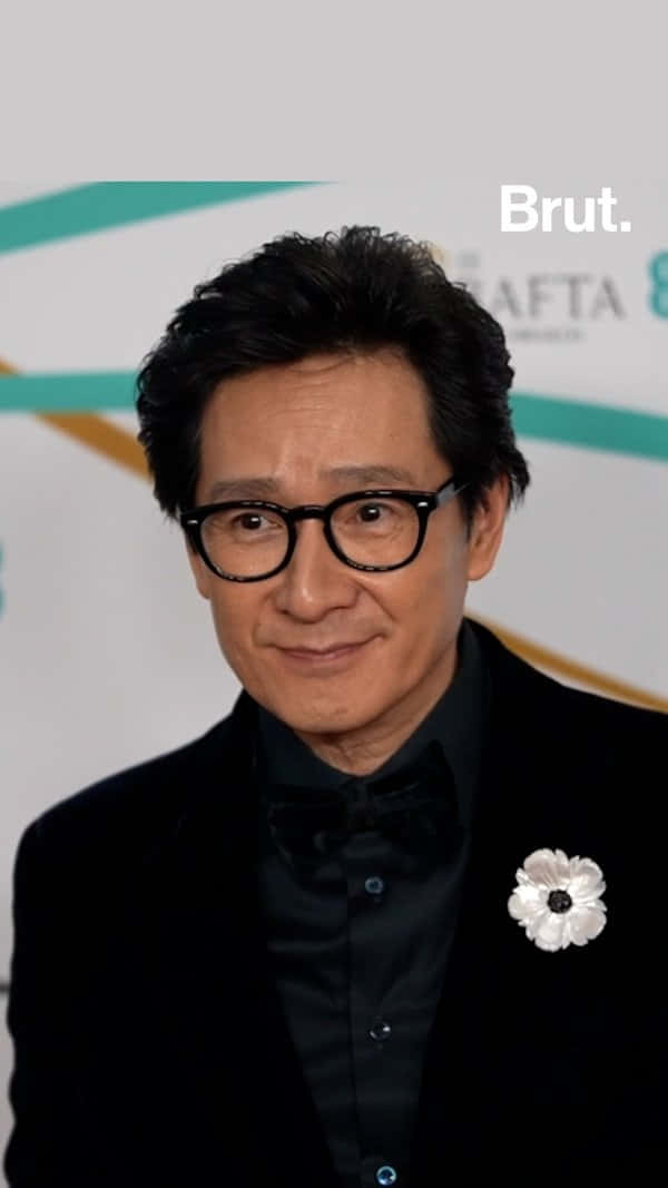 Ke Huy Quan 桌布 壁紙 — 一名身穿黑色燕尾服、佩戴白色襟花的男士在BAFTA活動中對著鏡頭微笑。