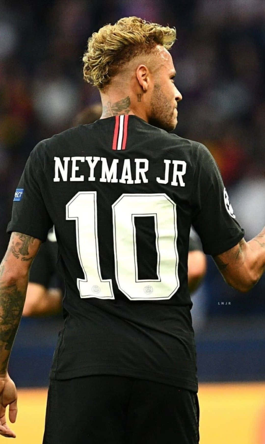 Neymar 桌布 壁紙 — 一名身穿黑色球衣、背後印有「NEYMAR JR」和10號的足球員站在球場上，背景是模糊的體育場燈光。