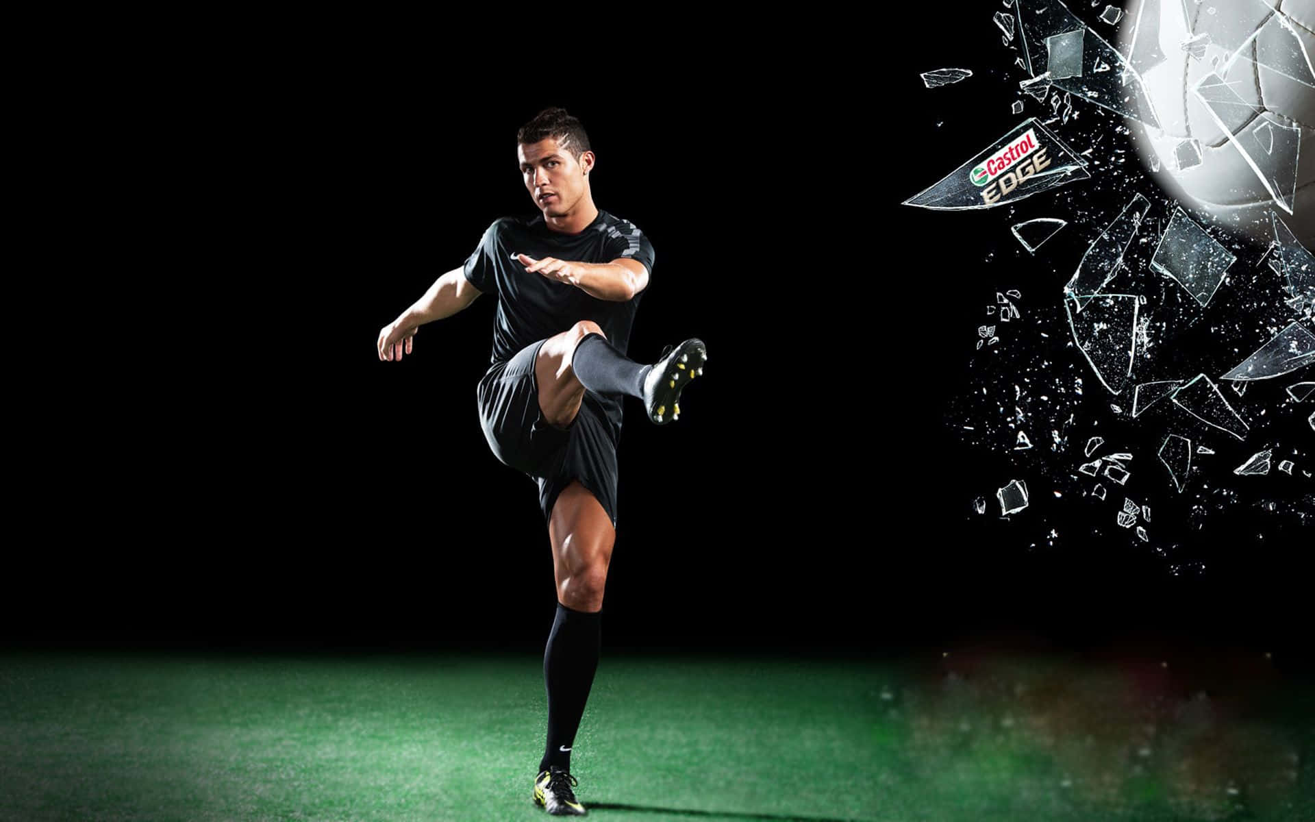 3d Sports 桌布 壁紙 — 一名身穿黑色球衣的足球員強力踢球，玻璃碎片從Castrol Edge標誌中爆裂開來，背景為深色。