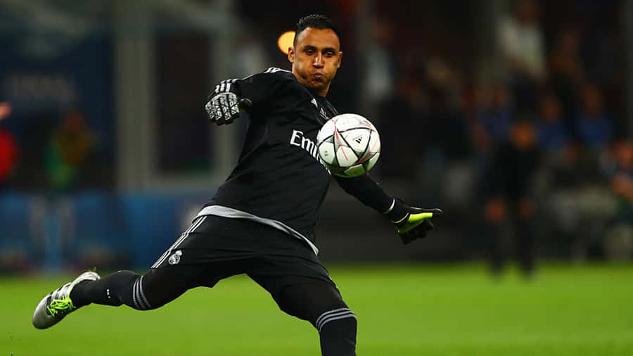 Keylor Navas 桌布 壁紙 — 一名身穿黑色球衣的足球守門員在球場燈光下於綠色草地上踢一個白色足球。