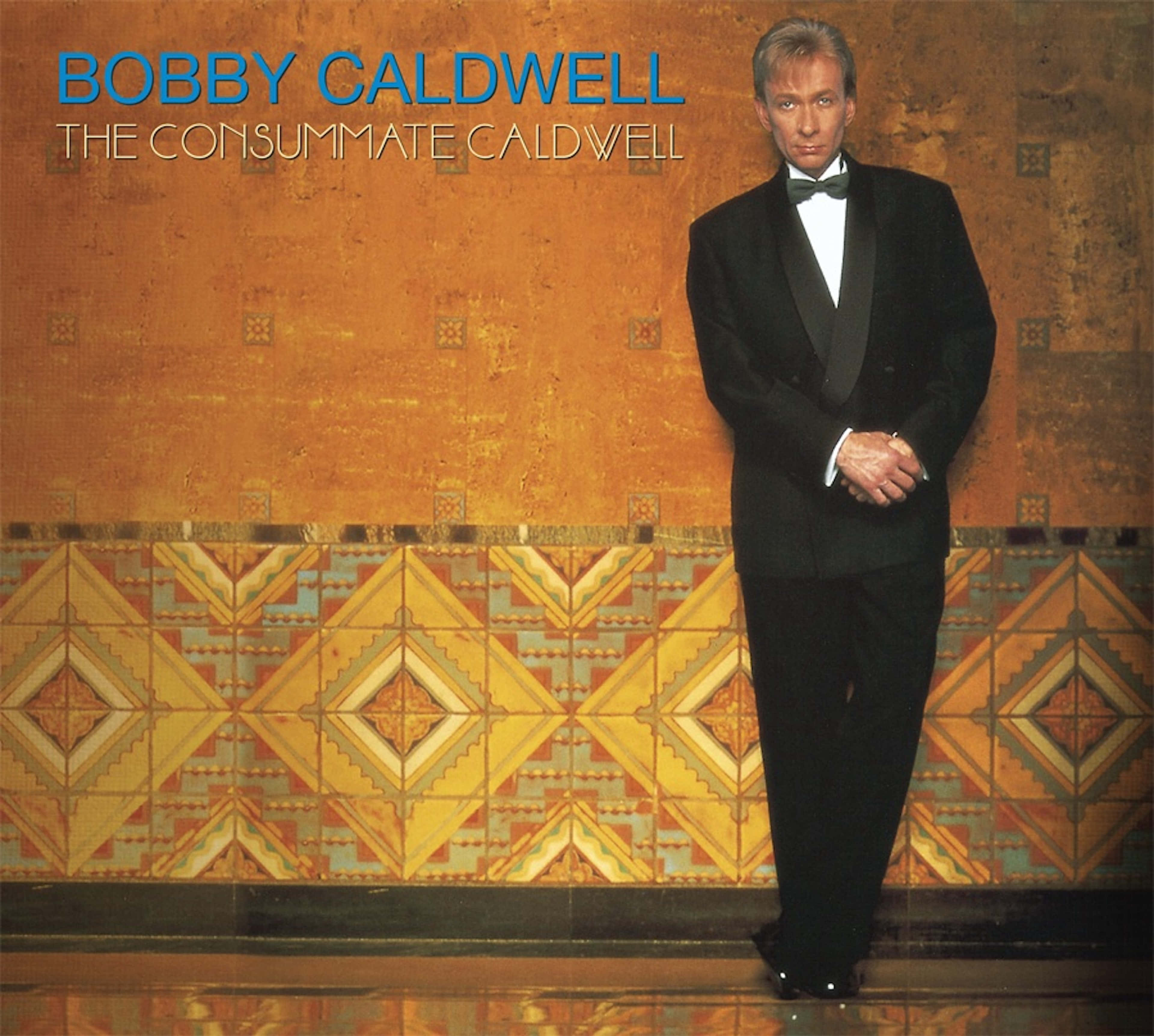 Bobby Caldwell 桌布 壁紙 — 一名身穿黑色禮服嘅男士，企喺暖色調嘅牆前面，牆上有幾何瓷磚圖案。