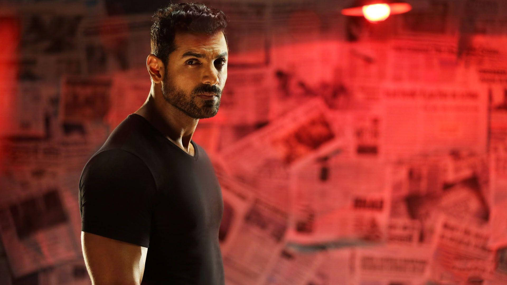 Bollywood HD 桌布 壁紙 — 一名身穿黑色襯衫的男子站在一個被報紙剪報包圍的紅色燈光房間裡。