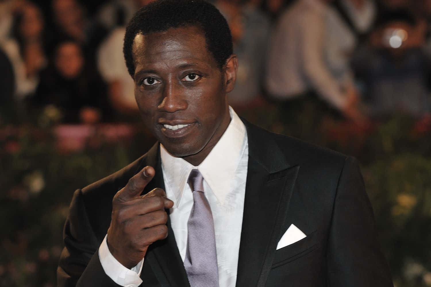 Wesley Snipes 桌布 壁紙 — 一名身穿黑色西裝和薰衣草色領帶的男子，在模糊的人群背景下，自信地微笑著直接指向相機。