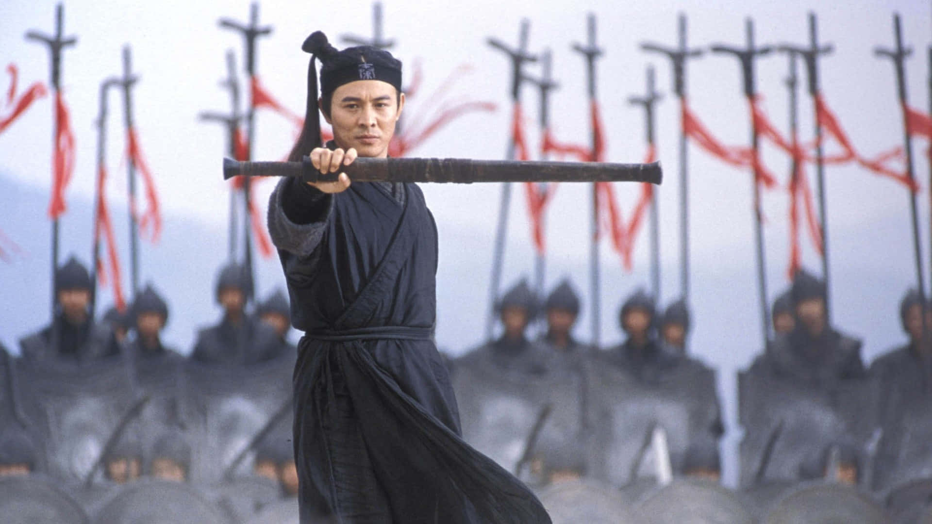 Samurai Movies 桌布 壁紙 — 一名身穿黑色長袍的戰士專注地向前舉起法杖，身後站著模糊的士兵，手持紅色旗幟。