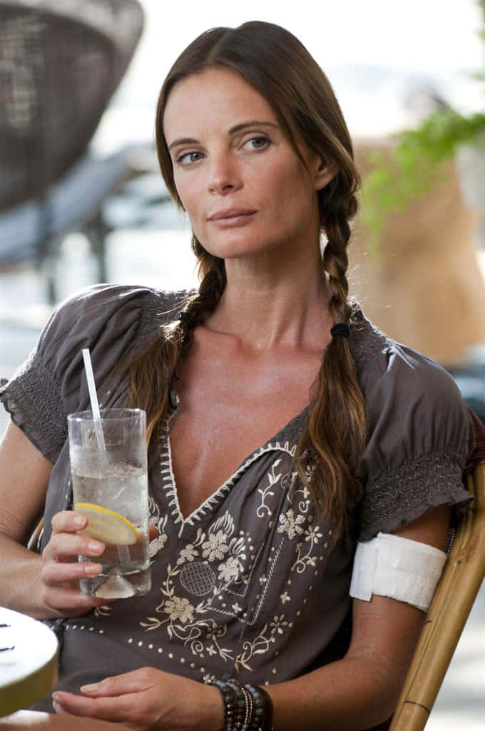 Gabrielle Anwar 桌布 壁紙 — 一名辮子髮型的女性坐在戶外，手臂上纏著繃帶，手持檸檬水飲料。