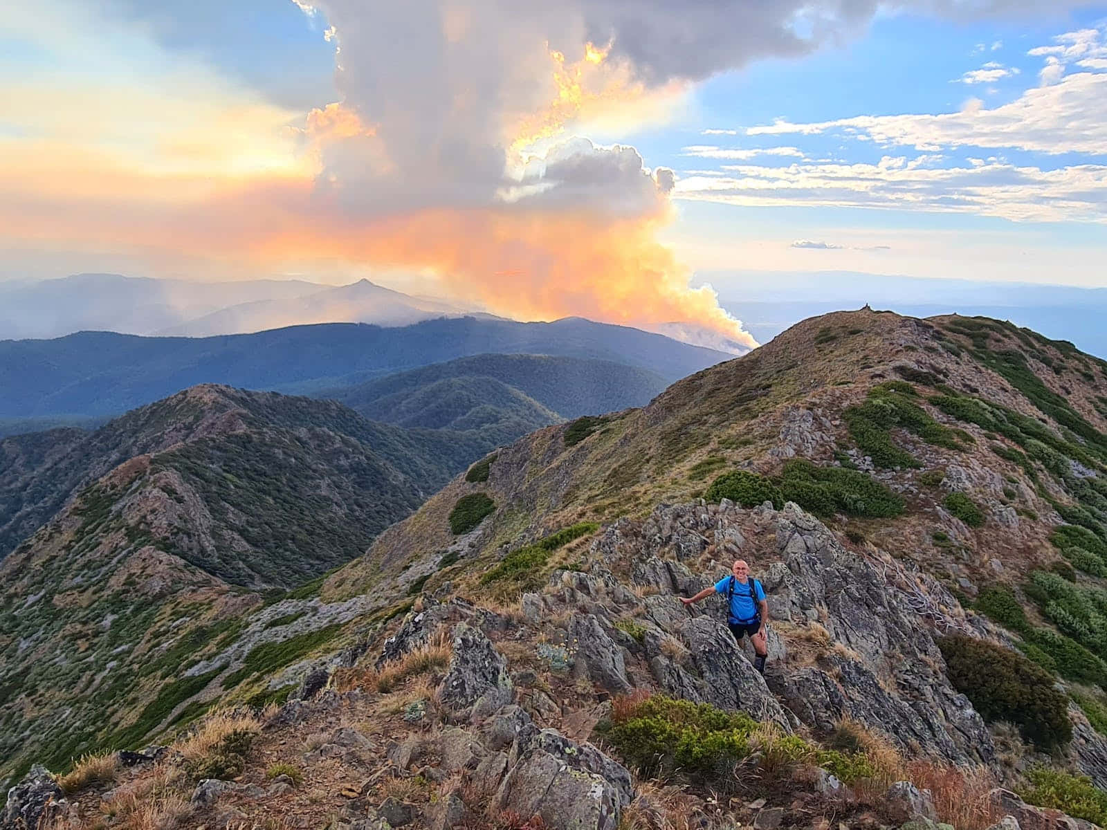 Hiking 桌布 壁紙 — 一名遠足者勝利地站在崎嶇的山脊上，熾熱的夕陽點燃了遠處山峰背後的雲彩。
