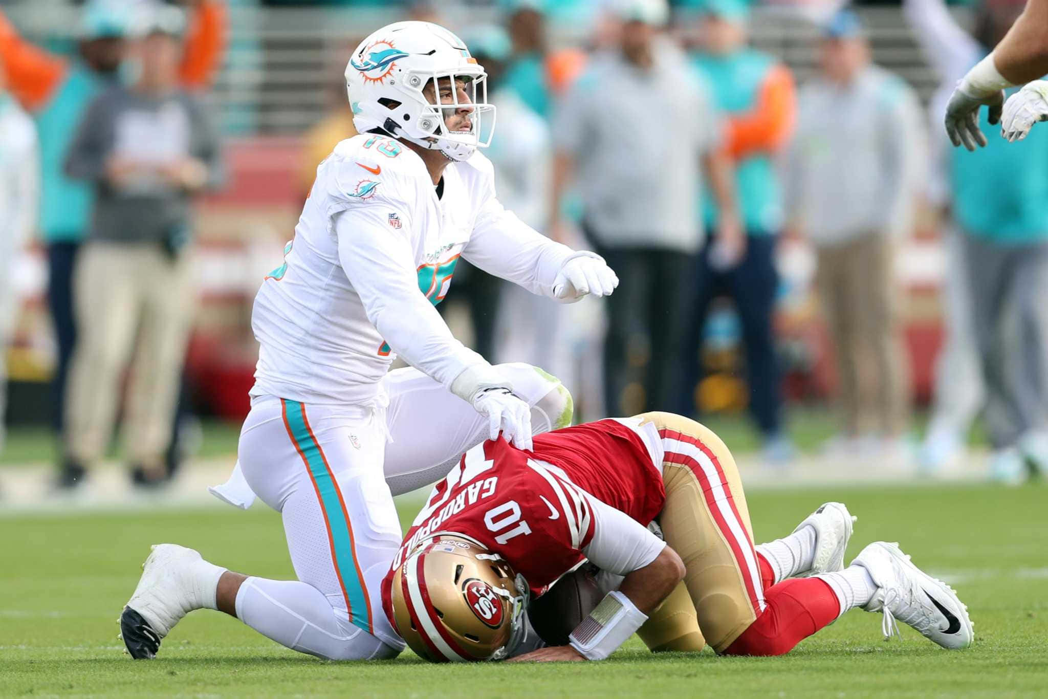 Jimmy Garoppolo 桌布 壁紙 — 一名邁阿密海豚隊球員在陽光明媚的足球場上跪在倒下的三藩市49人隊球員身上。