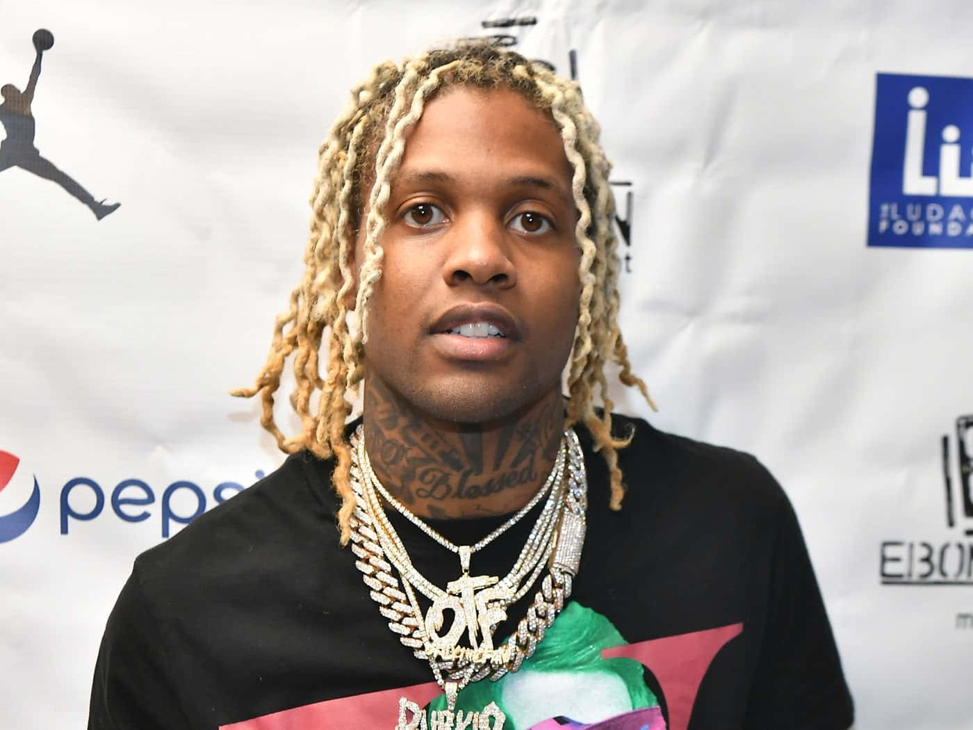 lil durk 桌布 壁紙 — 一名金髮辮子、戴著厚重金鏈的男子在印有百事可樂和佐敦標誌的品牌活動背景前擺姿勢。