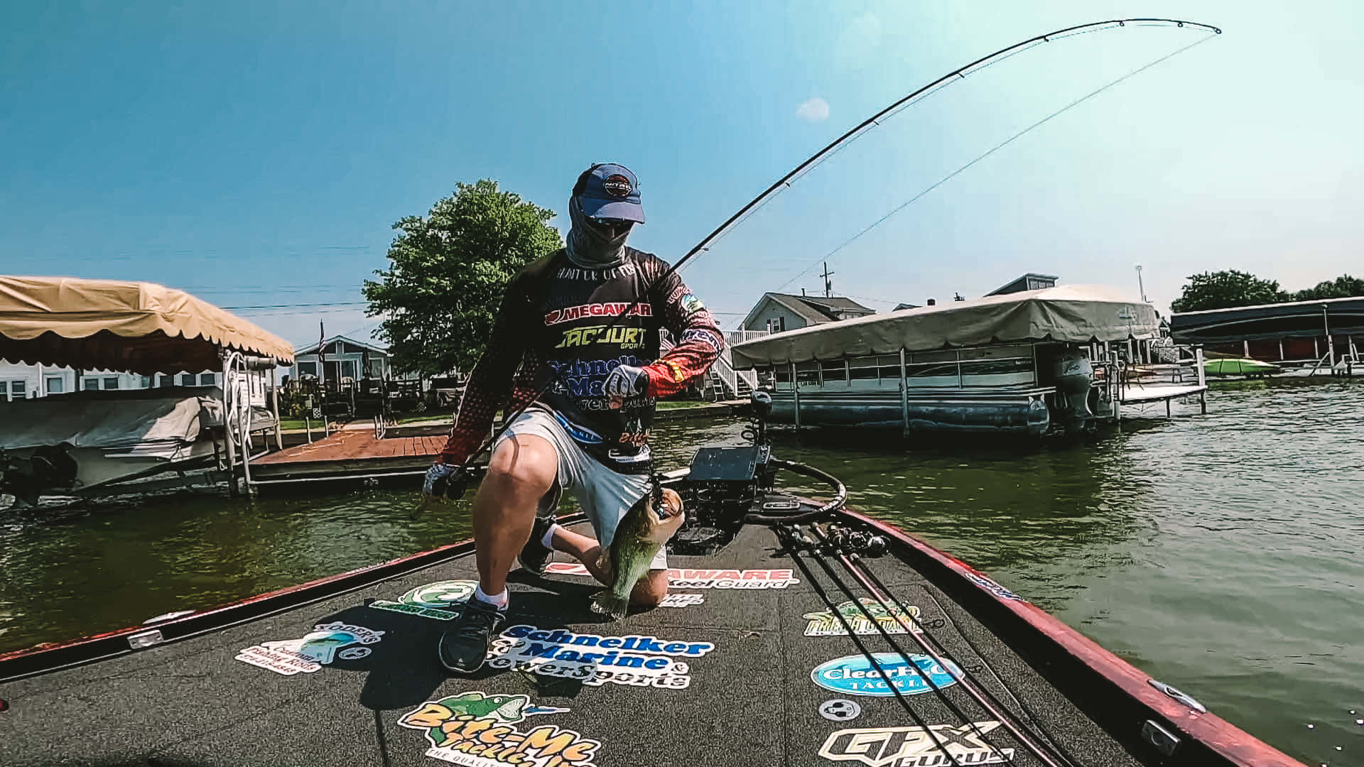 Fishing Rod 桌布 壁紙 — 一名釣魚人在鱸魚船上，在晴朗藍天下，背景有停泊的船隻和房屋，收線釣起一條大魚。
