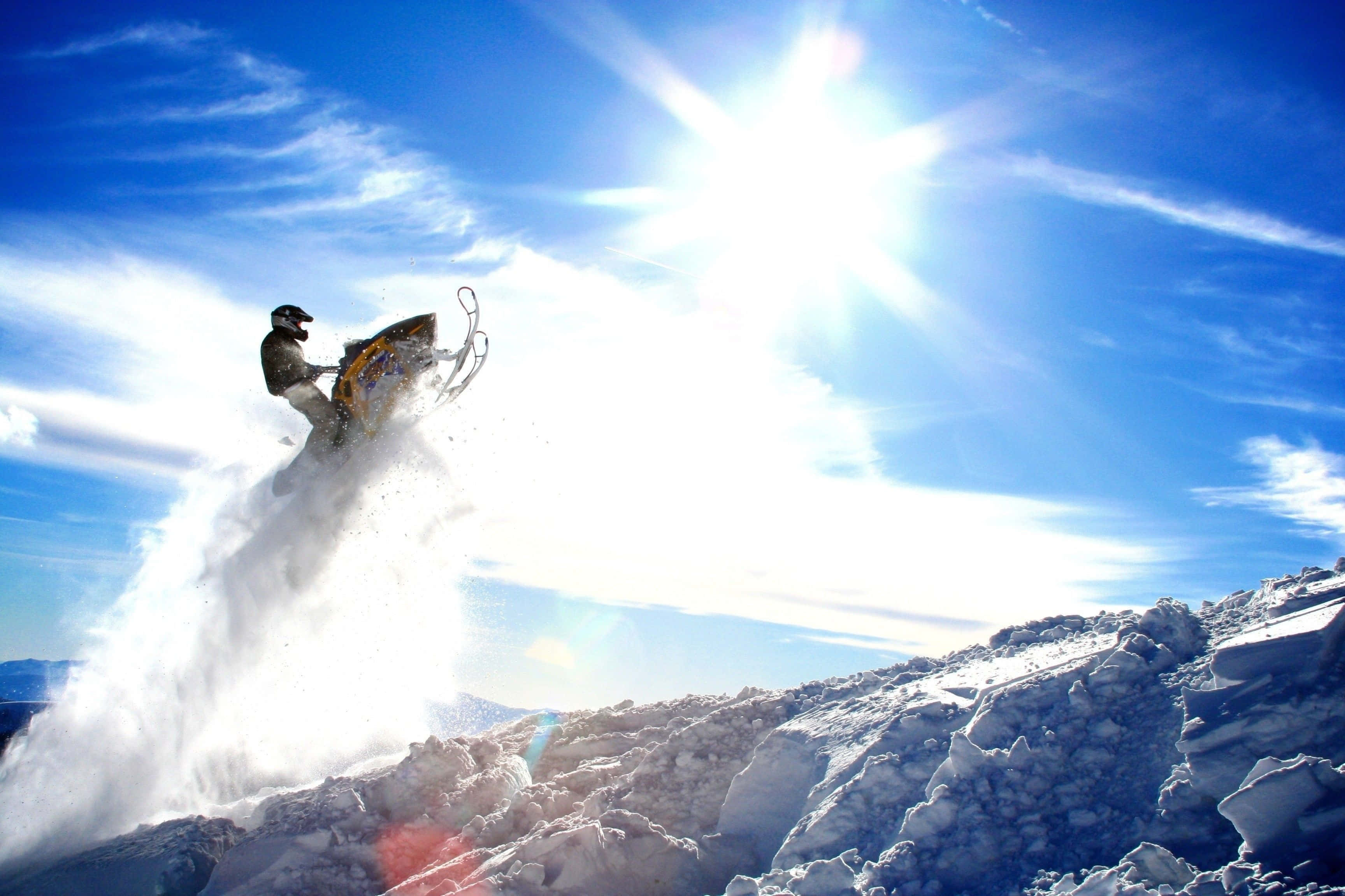 Winter Sports 桌布 壁紙 — 一名雪地電單車手在熾熱的陽光下，飛越白雪覆蓋的山脊。