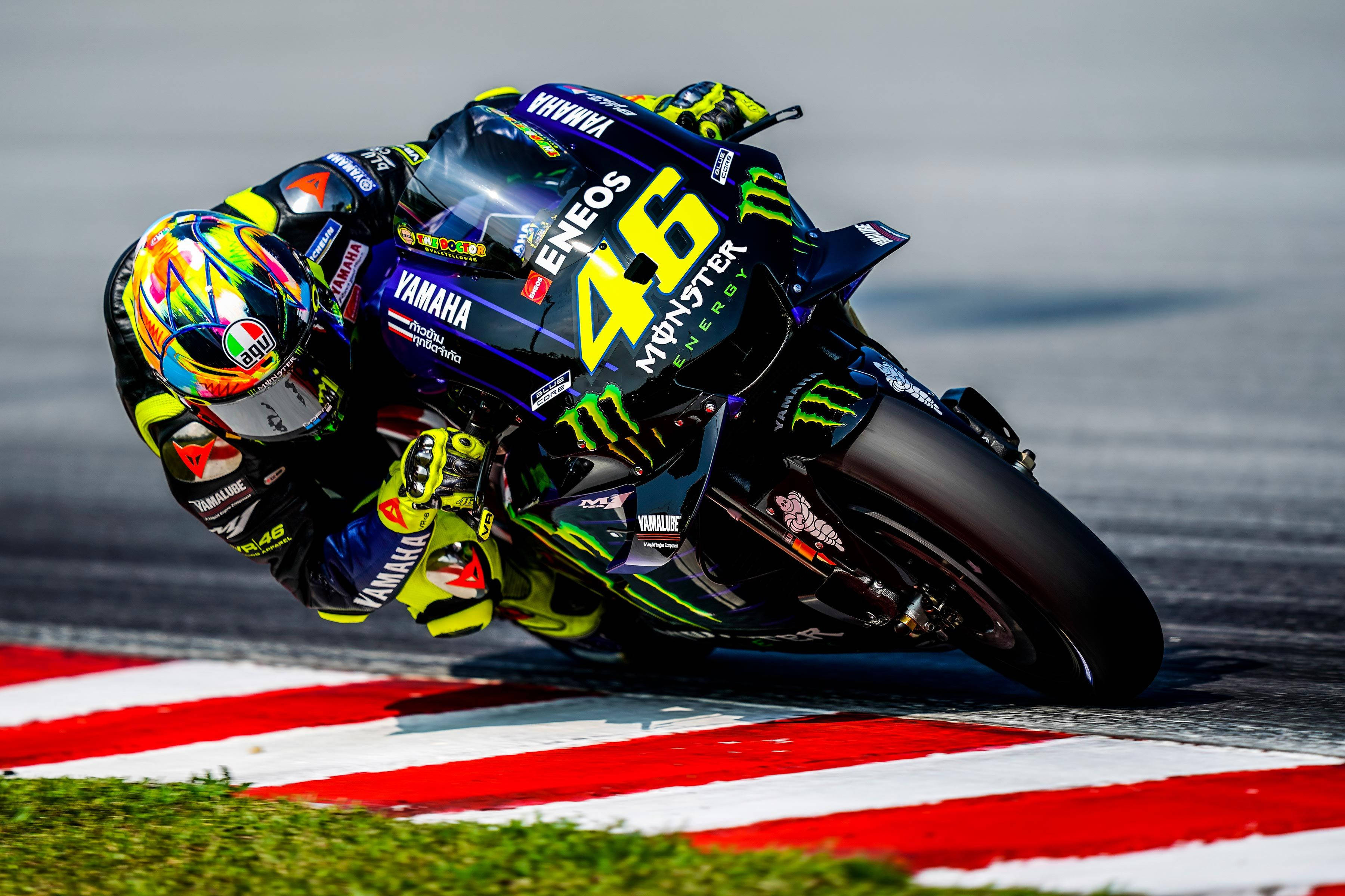 Monster Energy 桌布 壁紙 — 一名電單車手在賽道上急彎傾側，戴著鮮艷頭盔和帶有贊助商標誌的賽車服。