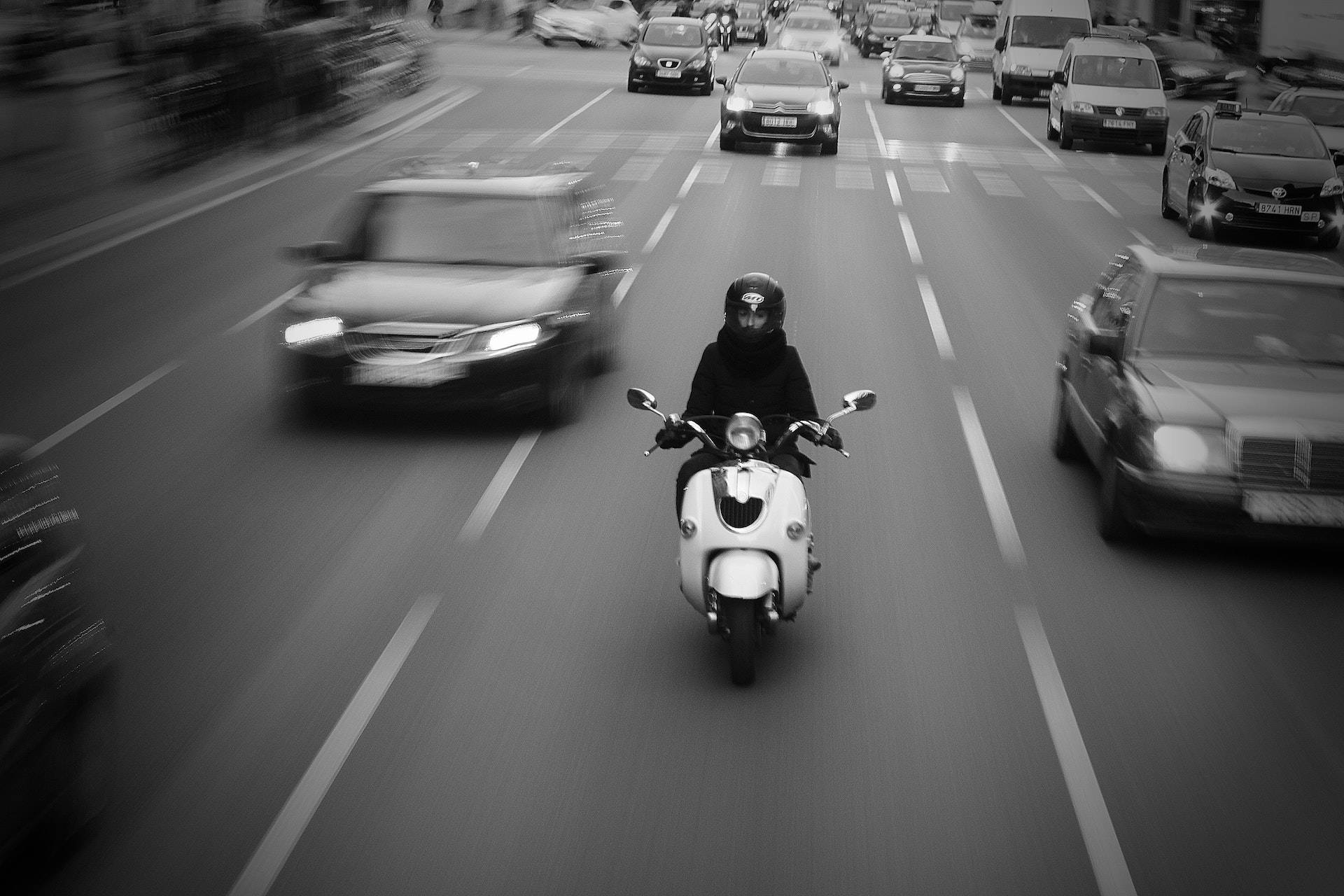 Speed 桌布 壁紙 — 一名電單車手騎著白色綿羊仔穿過繁忙的街道，背景有模糊的汽車，以黑白呈現。