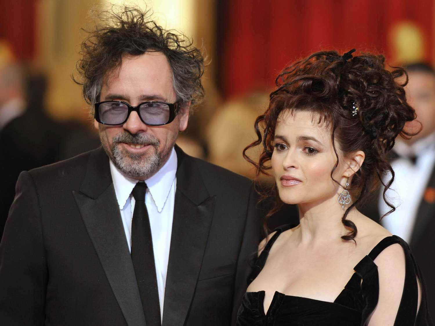 tim burton 桌布 壁紙 — 一名頭髮狂野、戴著深色眼鏡的男子，站在一位穿著黑色天鵝絨連衣裙、捲髮的女子旁邊，出席正式活動。