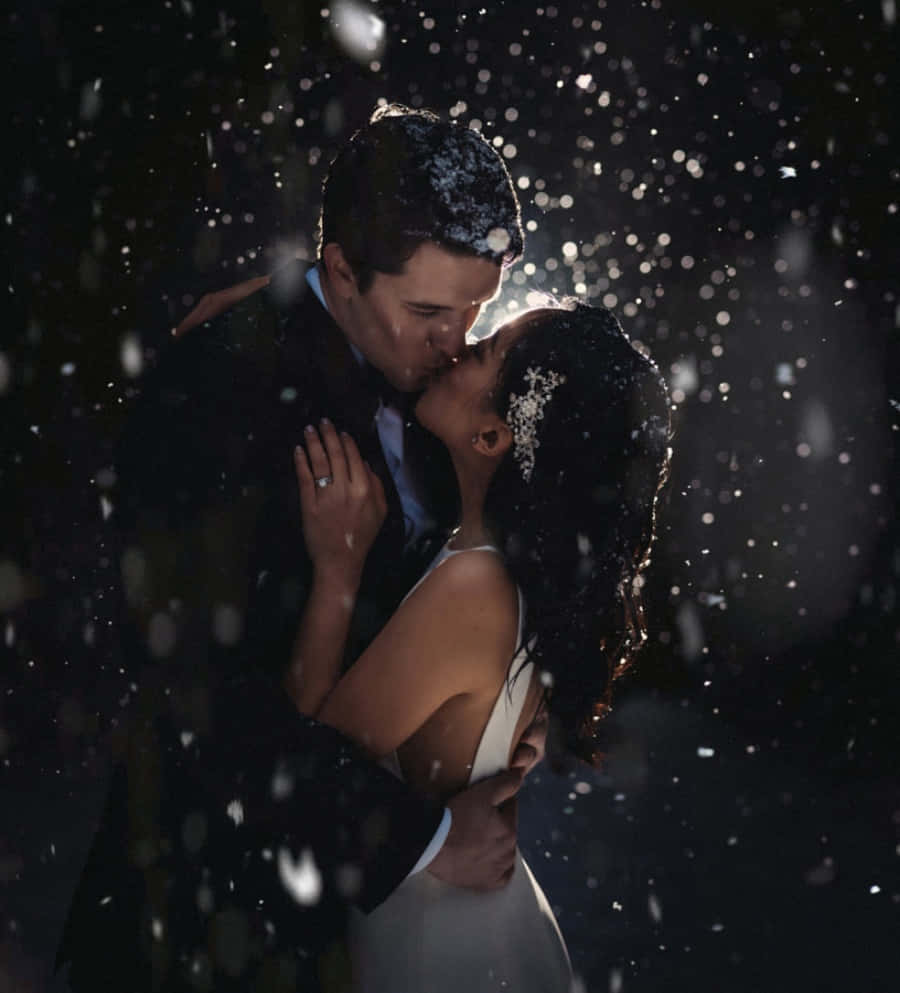 一吻激起幸福的浪漫時刻 壁紙 — 一對情侶在飄雪中親吻，柔和背光突顯他們的擁抱。