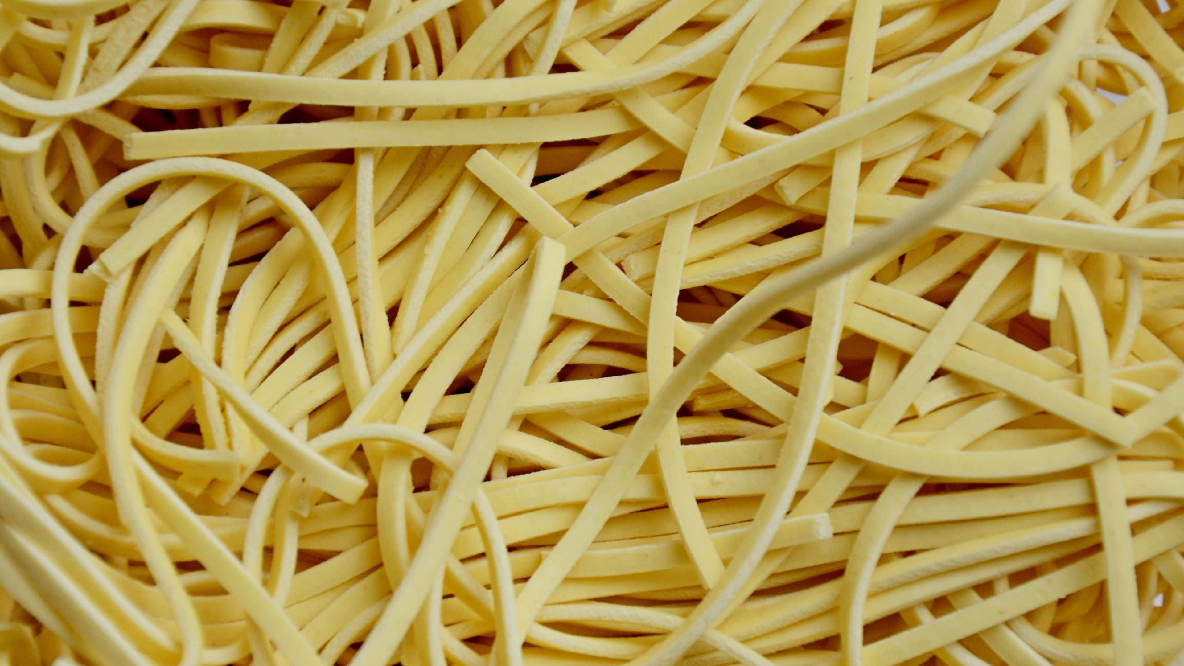Noodles 桌布 壁紙 — 一團淡黃色意粉絲纏繞在一起的特寫，營造出有紋理的食物背景。