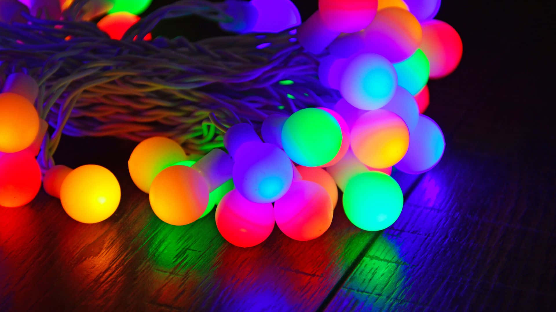 Glow In The Dark 桌布 壁紙 — 一團發光的彩色球形仙女燈在深色木質表面上投射出鮮豔的倒影。