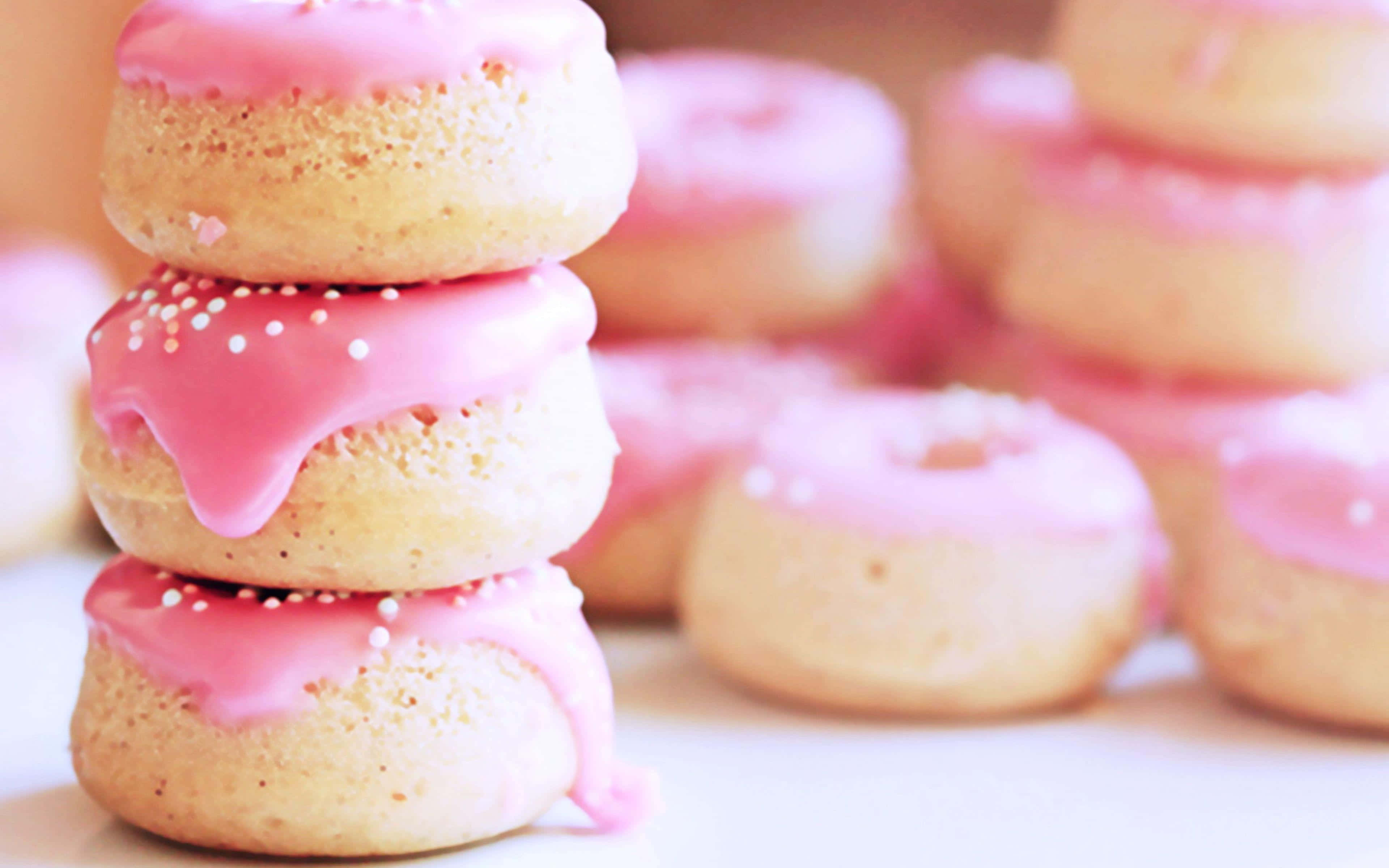 donuts 桌布 壁紙 — 一堆三個粉紅色糖霜甜甜圈，上面有白色糖粒，在模糊的粉彩甜甜圈背景下呈現柔和焦點。