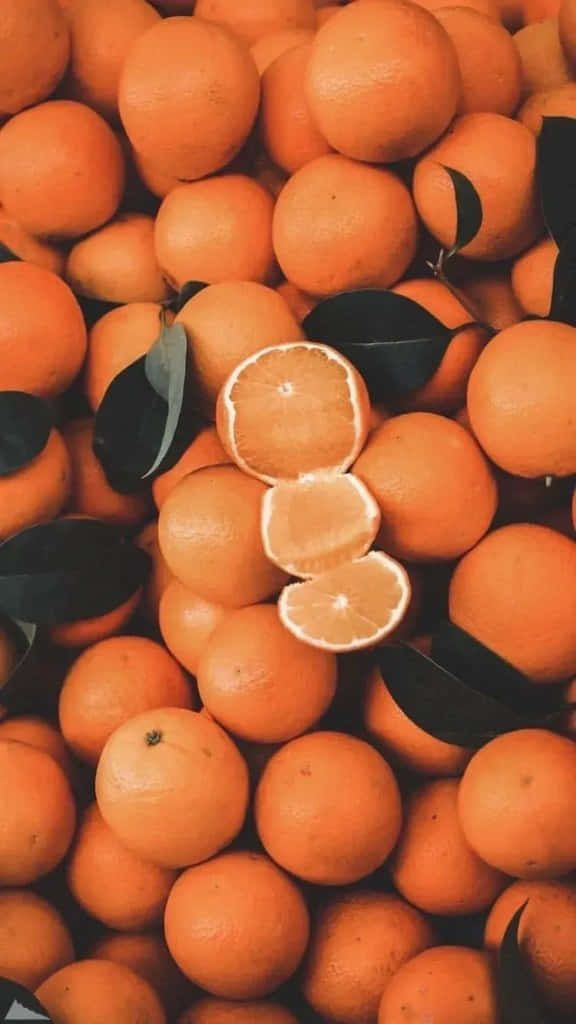 Cool Orange 桌布 壁紙 — 一堆充滿活力的完整和半個橙子，深色葉子散落各處。