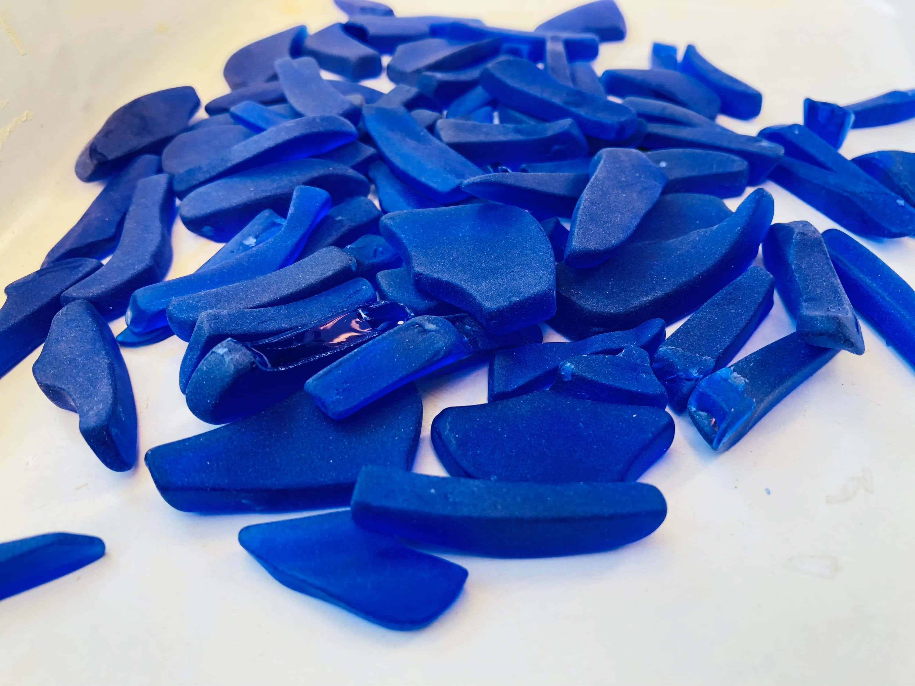 Cobalt Blue 桌布 壁紙 — 一堆充滿活力的鈷藍色海玻璃碎片散落在淡色表面上，光滑且風化的邊緣捕捉光線。