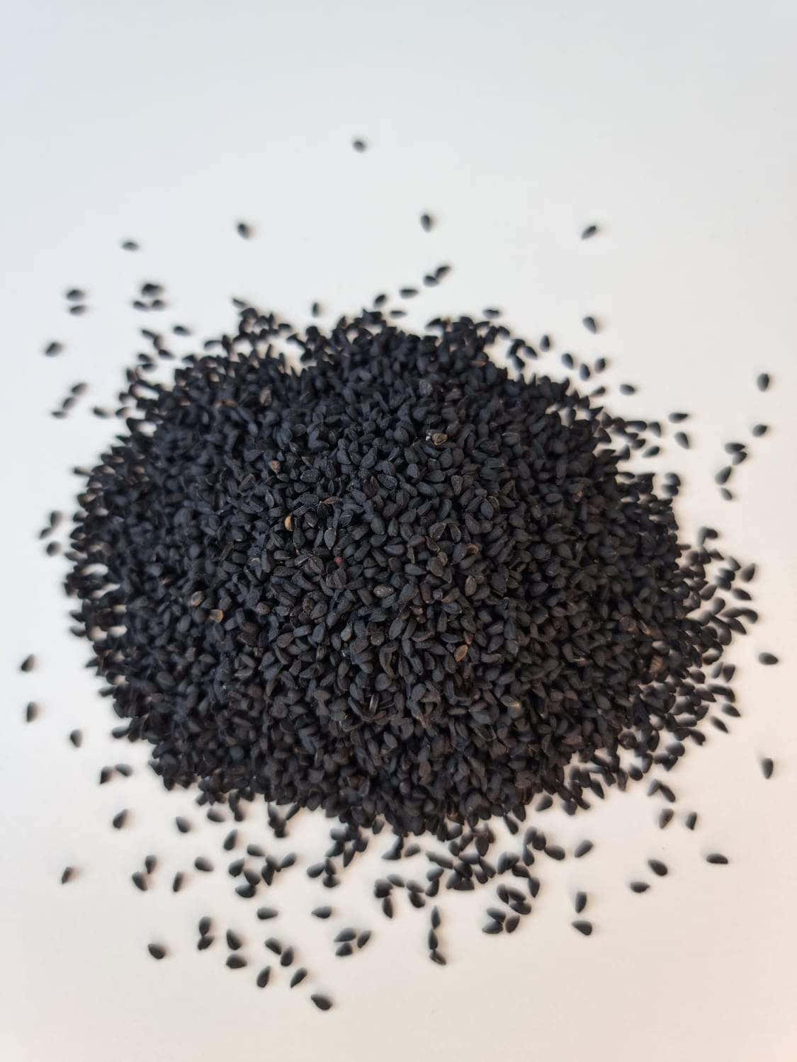 Black Cumin 桌布 壁紙 — 一堆光澤黑芝麻散落在純白表面上的特寫。