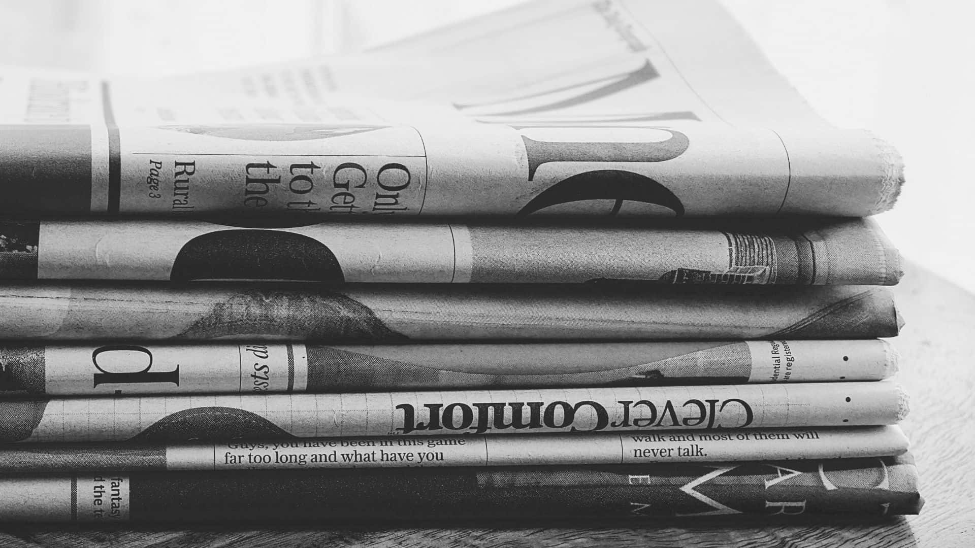 Black And White Newspaper 桌布 壁紙 — 一堆摺疊的黑白報紙放在木質表面上，可見標題和文字。