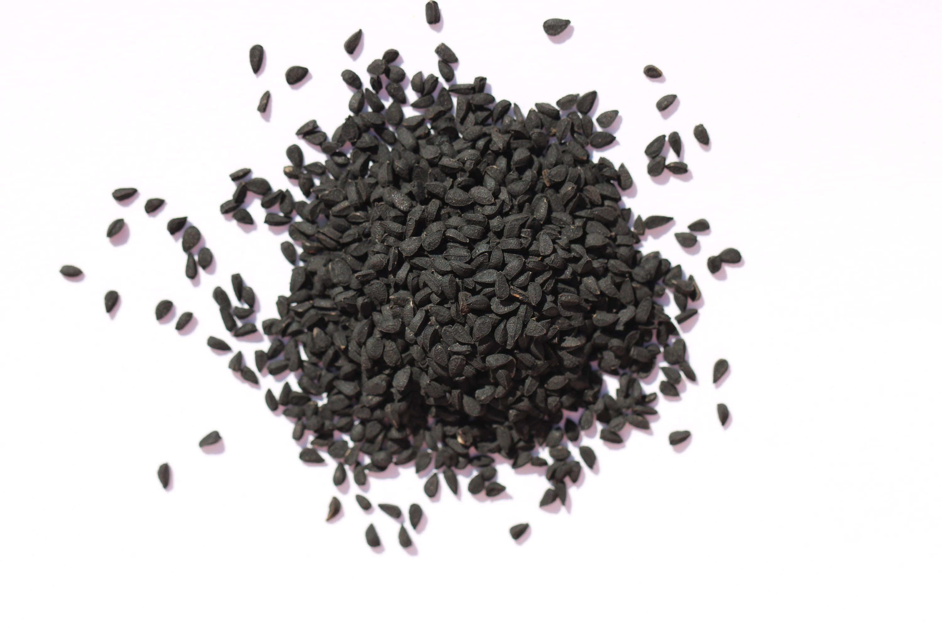 Black Cumin 桌布 壁紙 — 一堆有光澤的黑芝麻散落在明亮的白色表面上，帶有柔和的陰影。