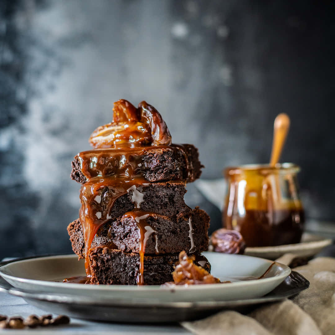 Caramel Brownie 桌布 壁紙 — 一堆濃郁的朱古力布朗尼，淋上閃亮的焦糖醬，並以焦糖化山核桃點綴。