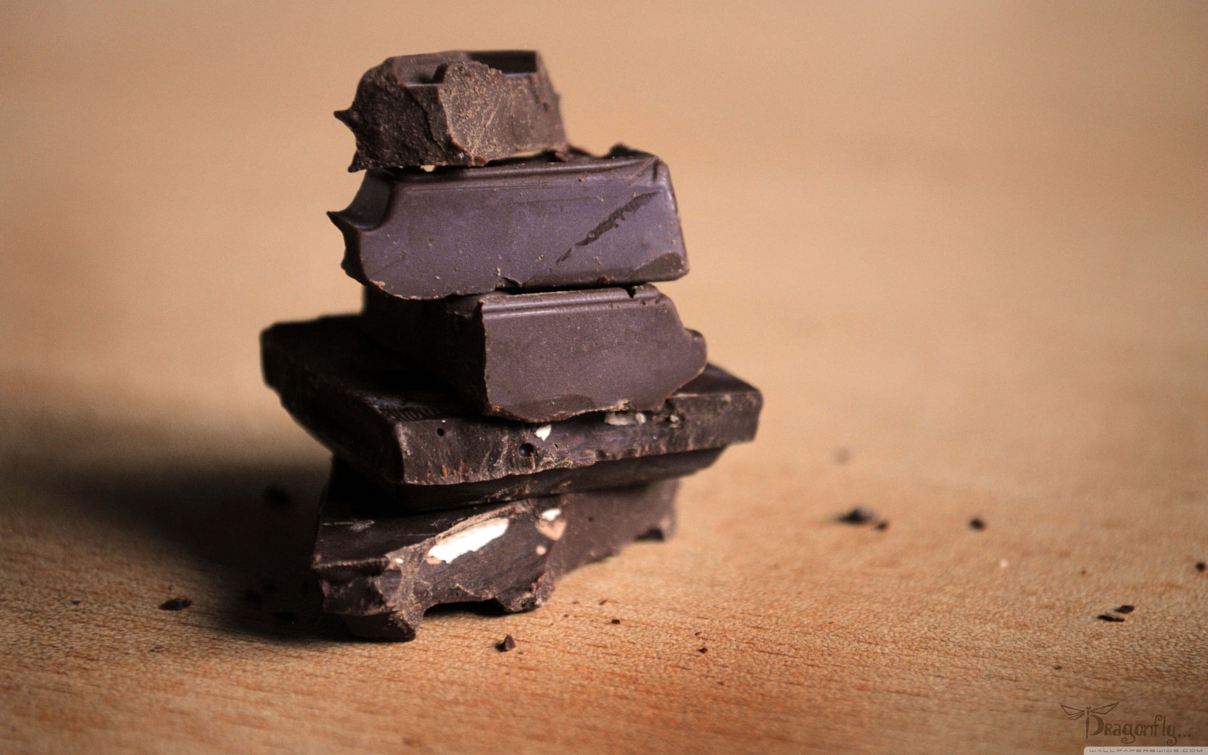 Dark Chocolate 桌布 壁紙 — 一堆粗糙的黑朱古力塊放在溫暖的木質表面上，帶有柔和淺景深效果。