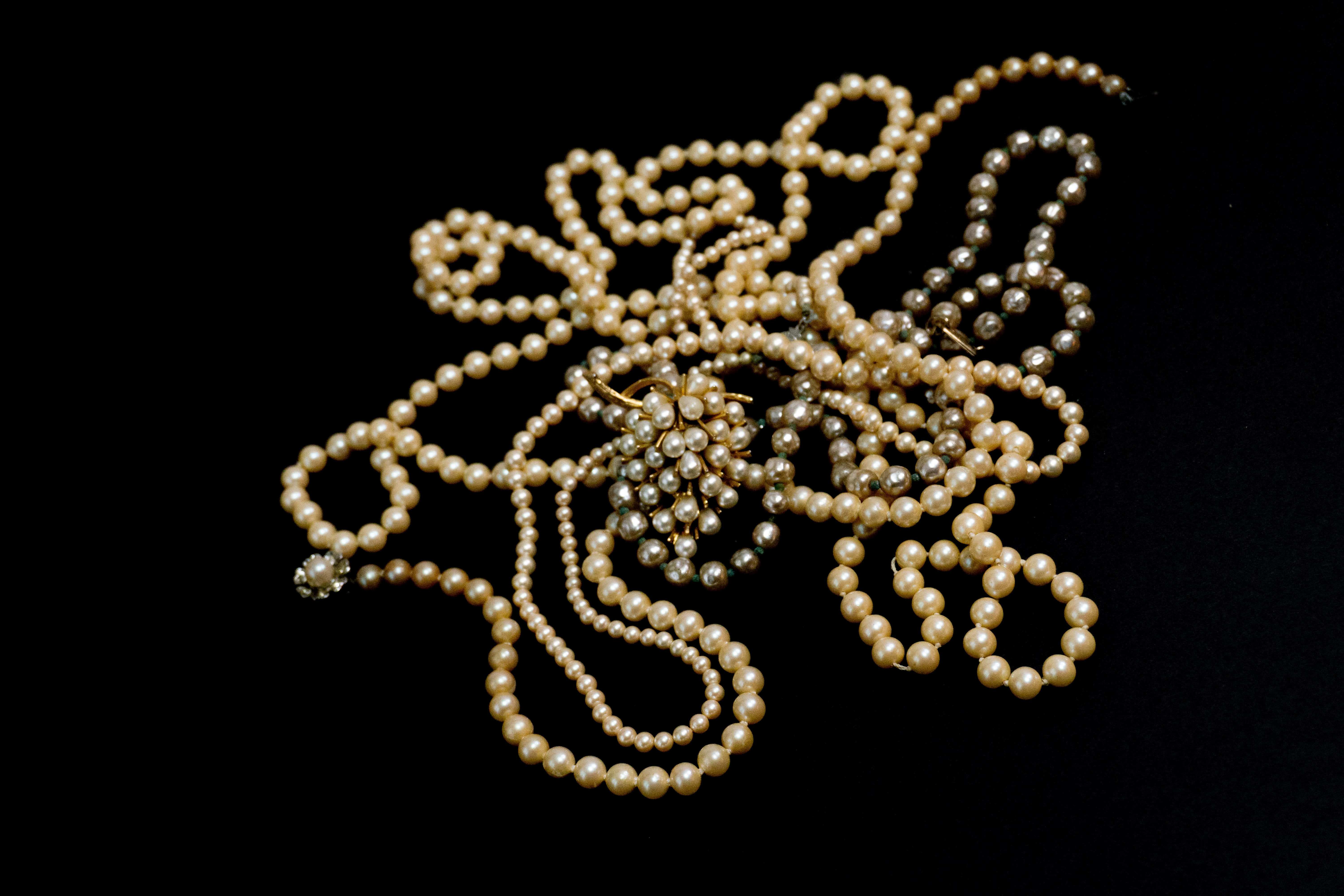 pearl 桌布 壁紙 — 一堆纏繞的奶油色和銀色珍珠，配以金色胸針，在純黑背景上呈現。