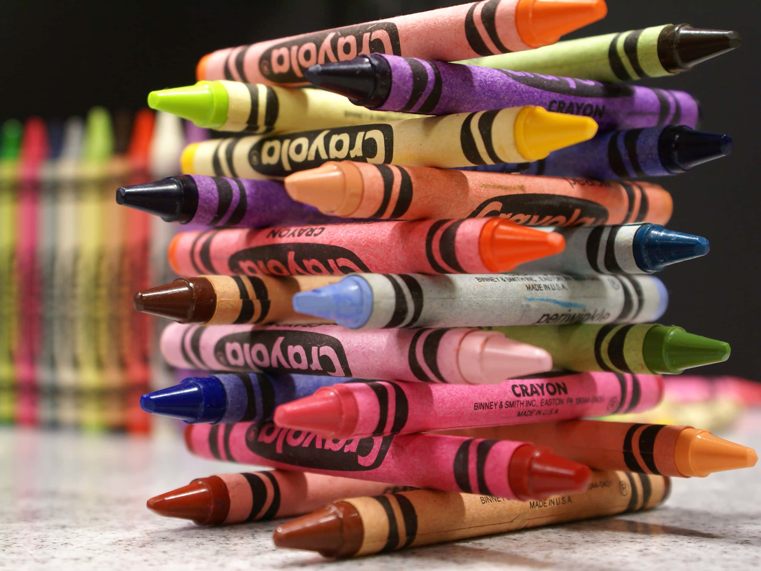 crayon 桌布 壁紙 — 一堆色彩繽紛的Crayola蠟筆以不同顏色搖搖欲墜地靠在有斑點的櫃檯上，背景蠟筆模糊不清。